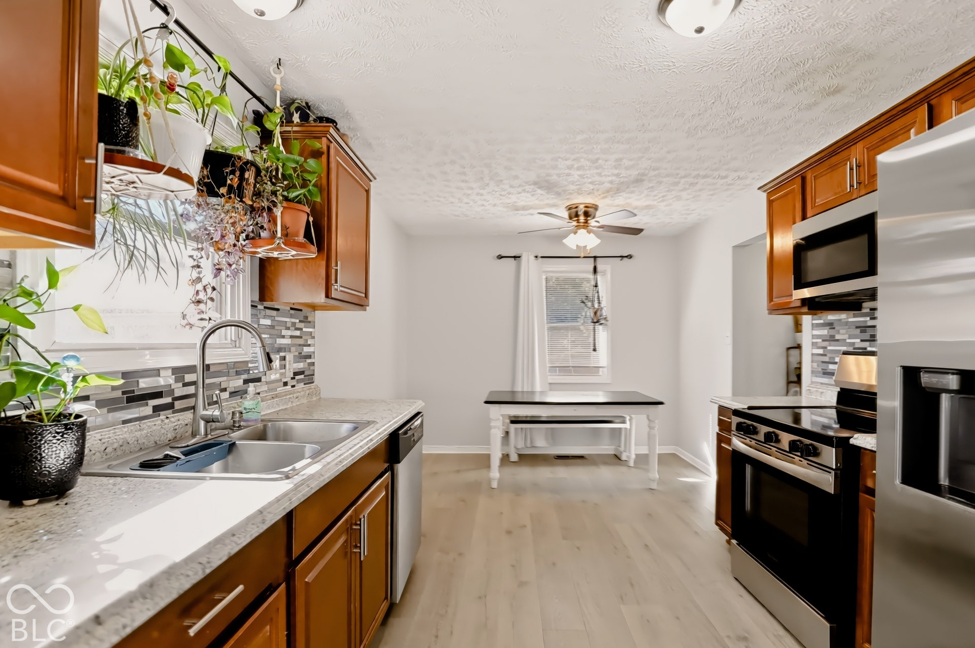 Kitchen featuring wood-finish cabinetry, stone-texture countertops, mosaic tile backsplash, stainless steel appliances, and wood-finish flooring