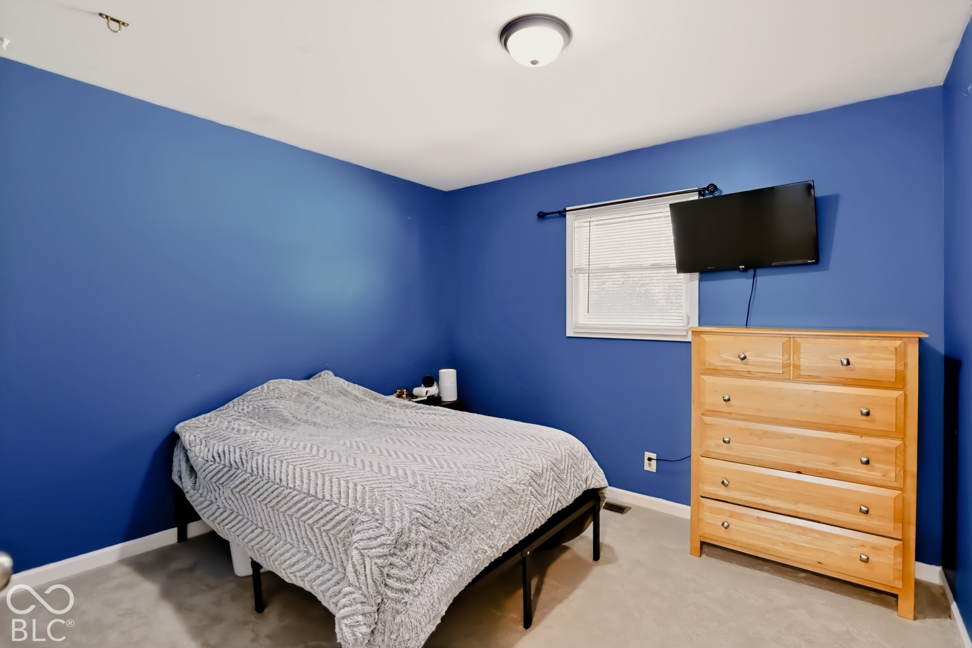 Neutral carpeting, single-hung window with installed curtain rod, and ceiling-mounted flush light fixture