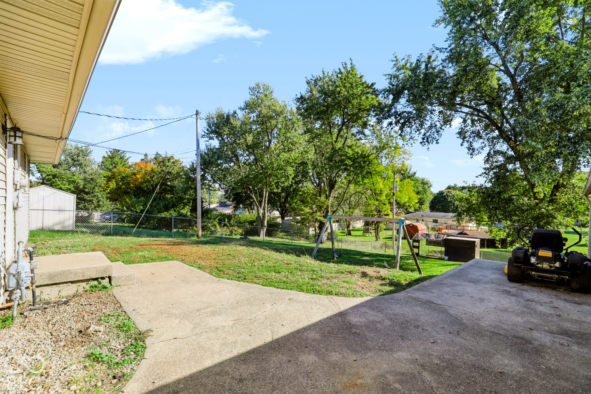 Rear yard featuring a concrete patio, chain-link perimeter fencing, detached metal storage shed, and mature trees