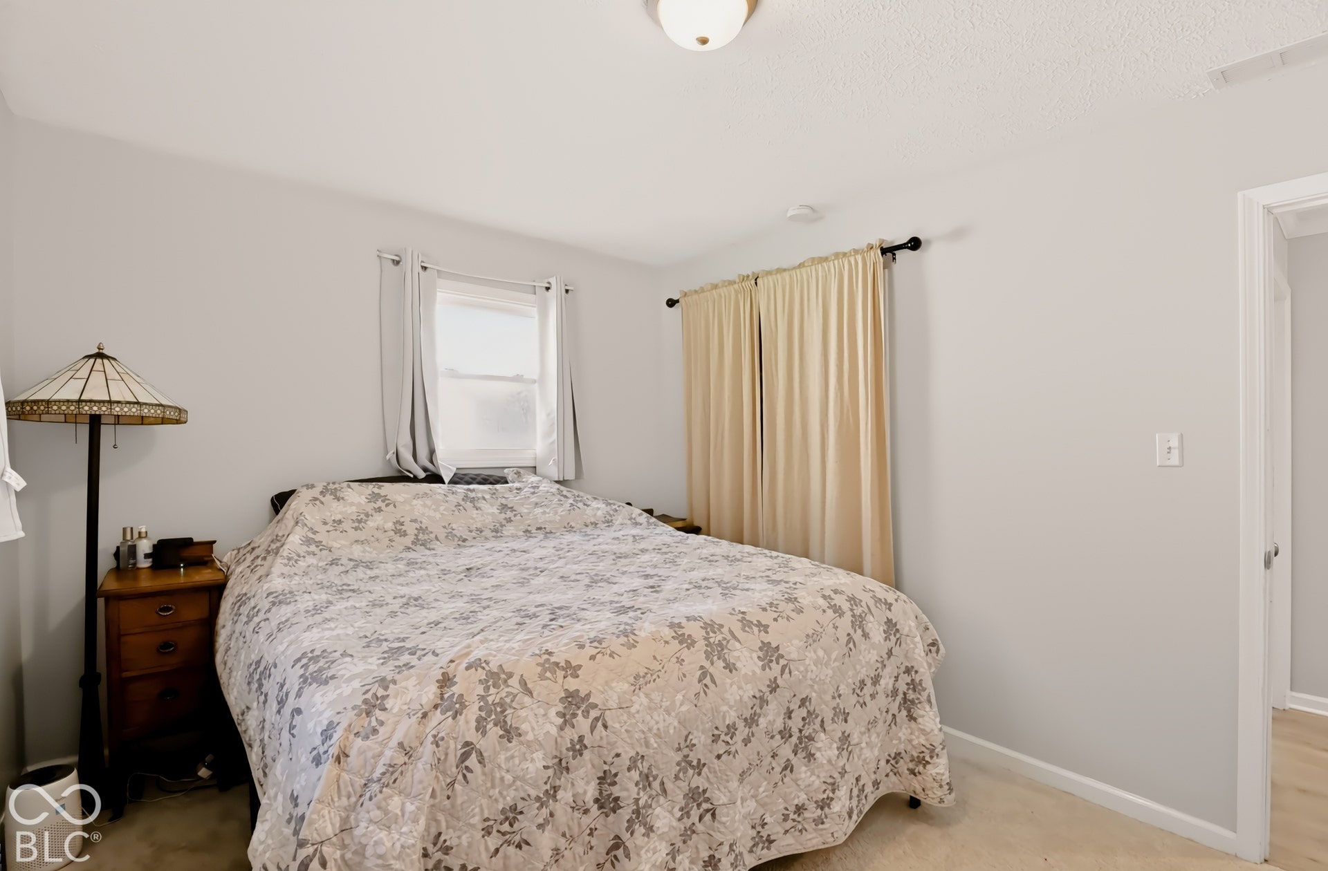 Neutral-toned walls, ceiling-mounted light fixture, and window openings with curtain rods