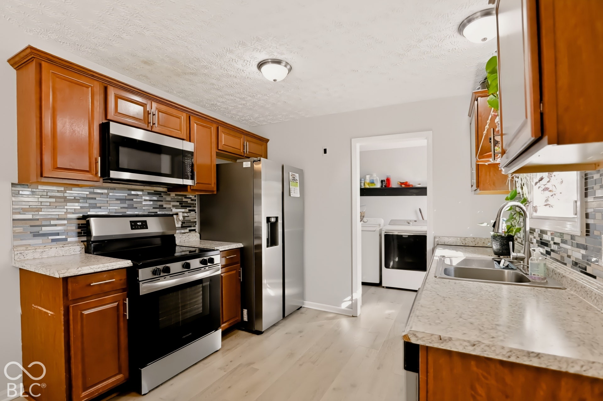 Kitchen featuring wood cabinetry, stainless steel appliances, speckled stone-finish countertops, and multi-tone glass tile backsplash
