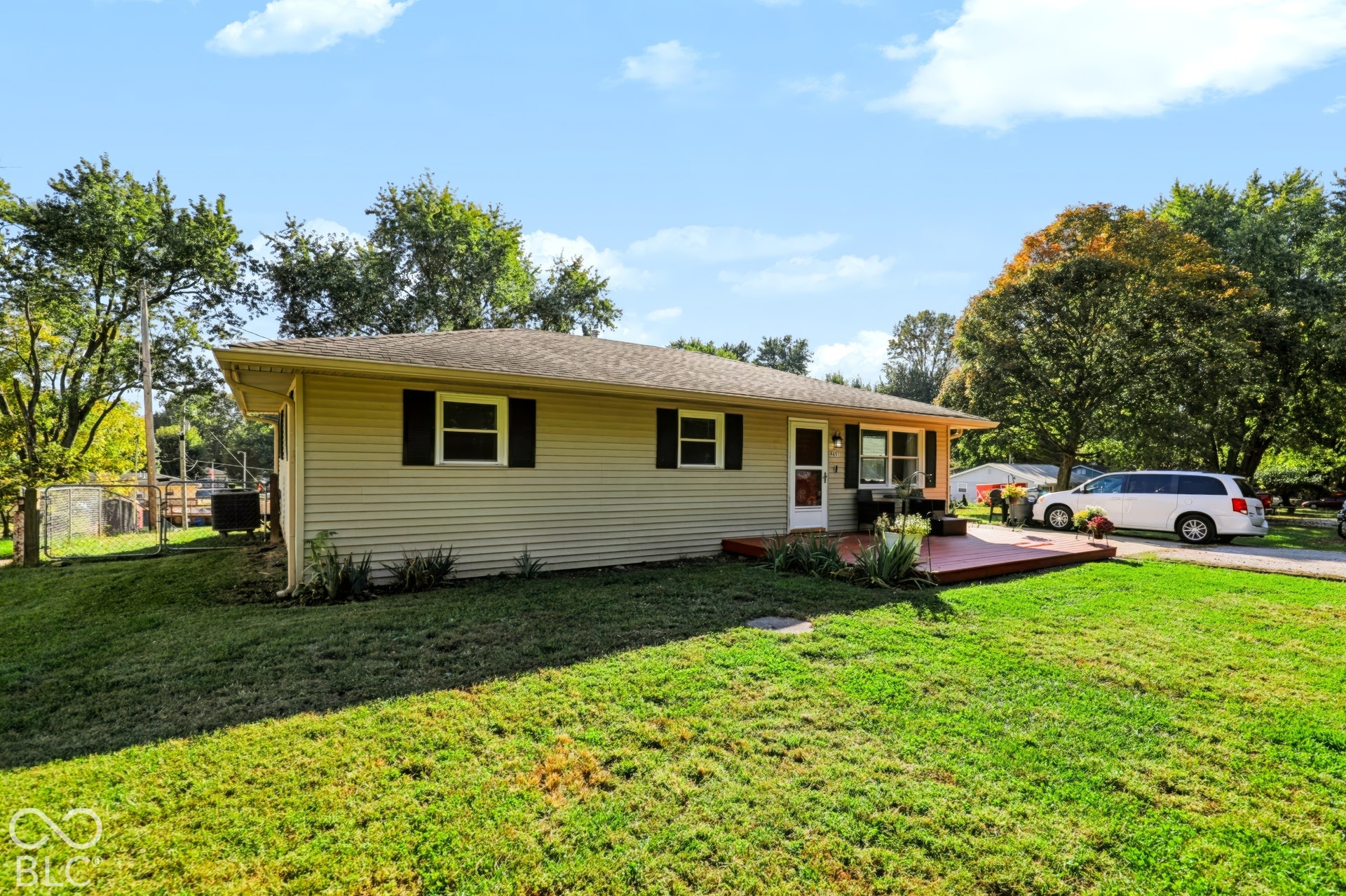 Single-story exterior featuring tan horizontal siding, dark window shutters, a hipped roofline, and a raised wooden deck