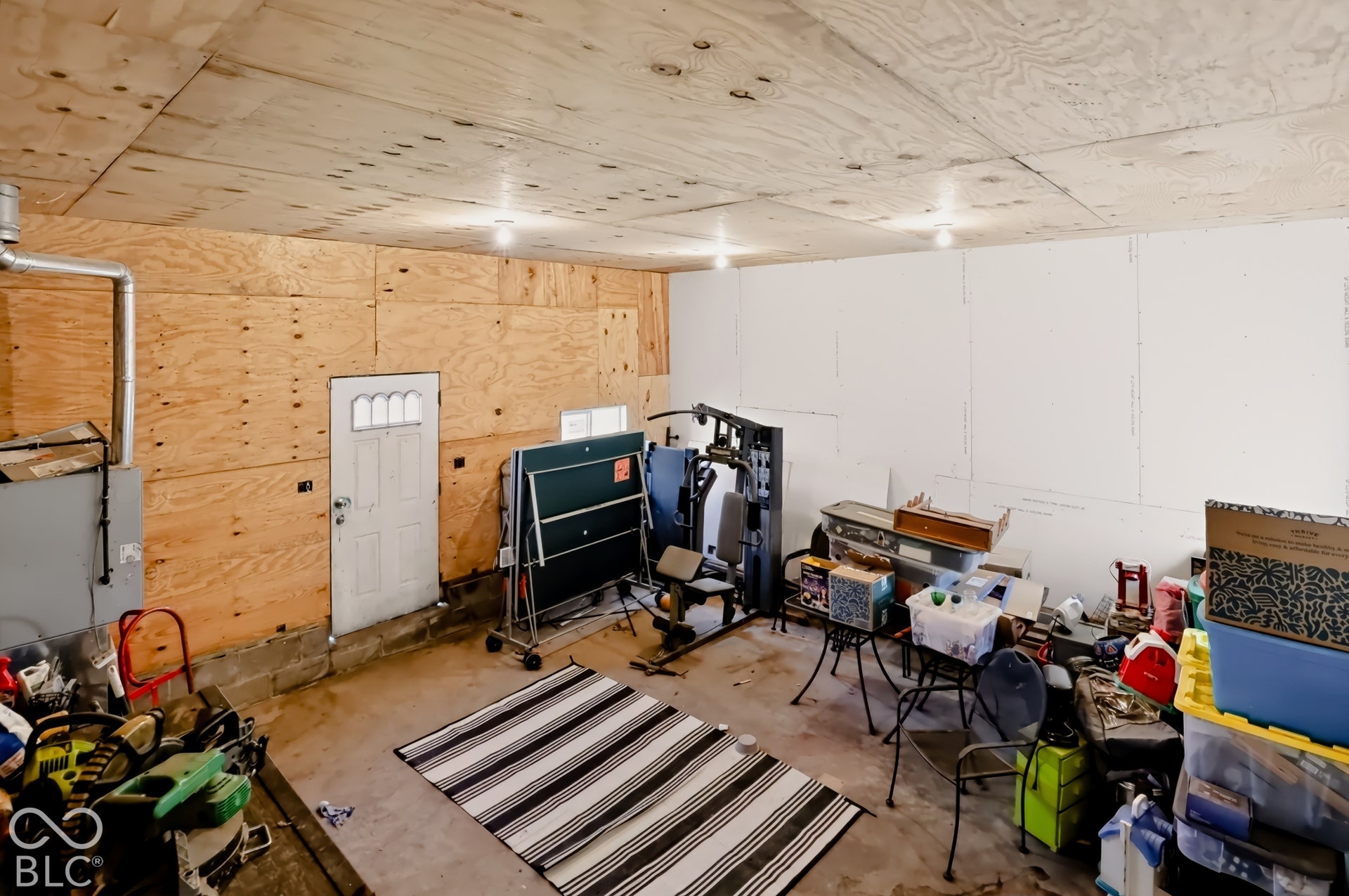 Enclosed space featuring plywood wall paneling, drywall finish, ceiling-mounted lighting, and a single exterior access door