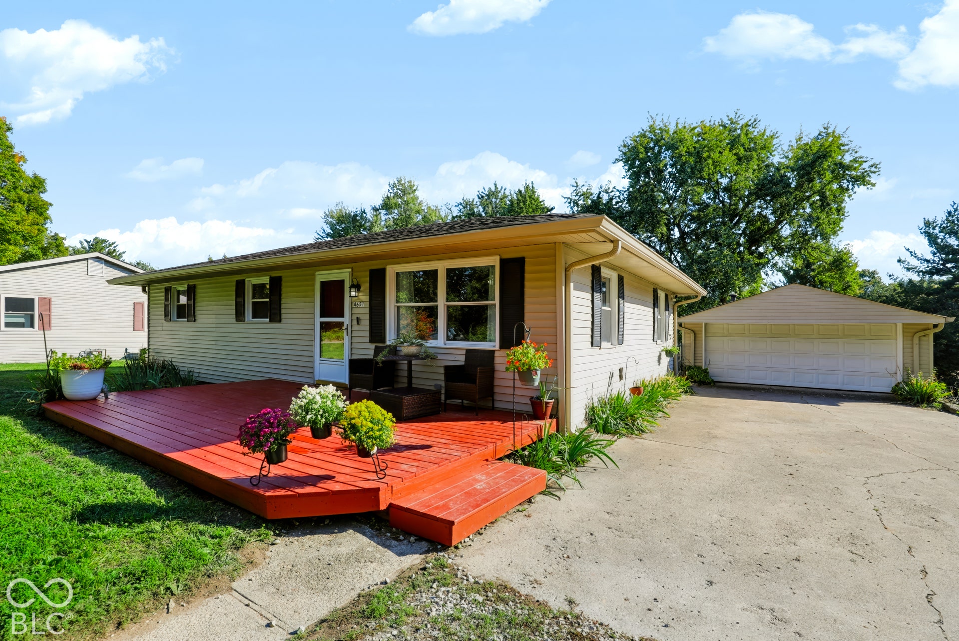 Single-story exterior featuring light-colored horizontal siding, a stained wood deck, an attached multi-car garage, and a concrete driveway
