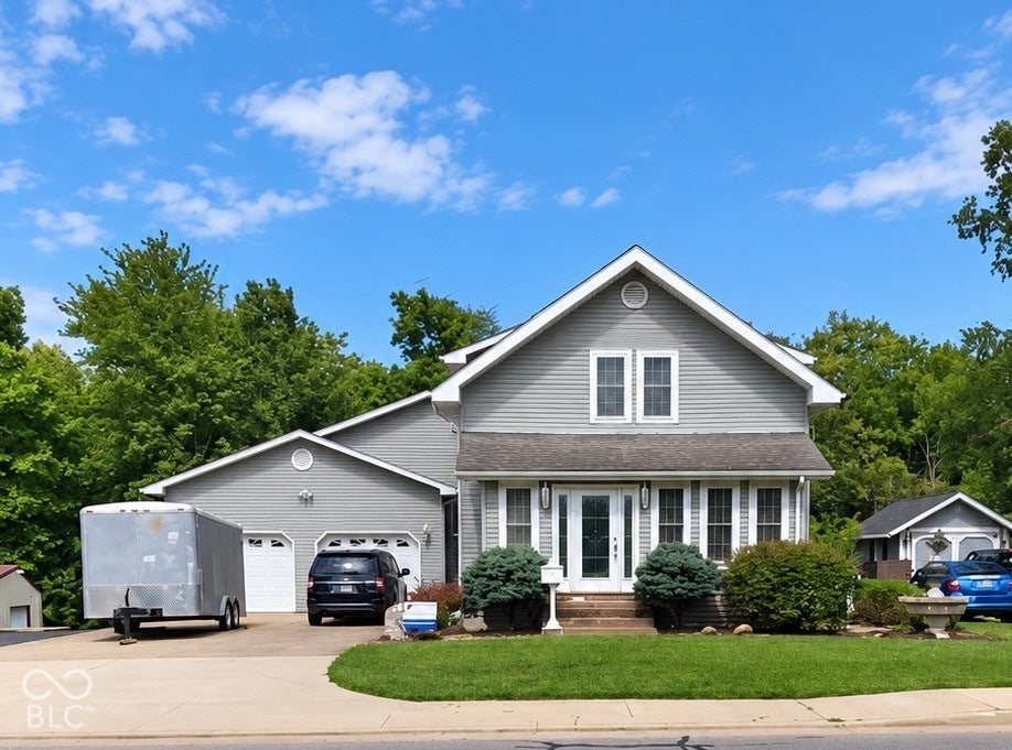 Traditional two-story exterior featuring light-toned horizontal siding, a gabled roofline, an attached two-car garage, and manicured landscaping