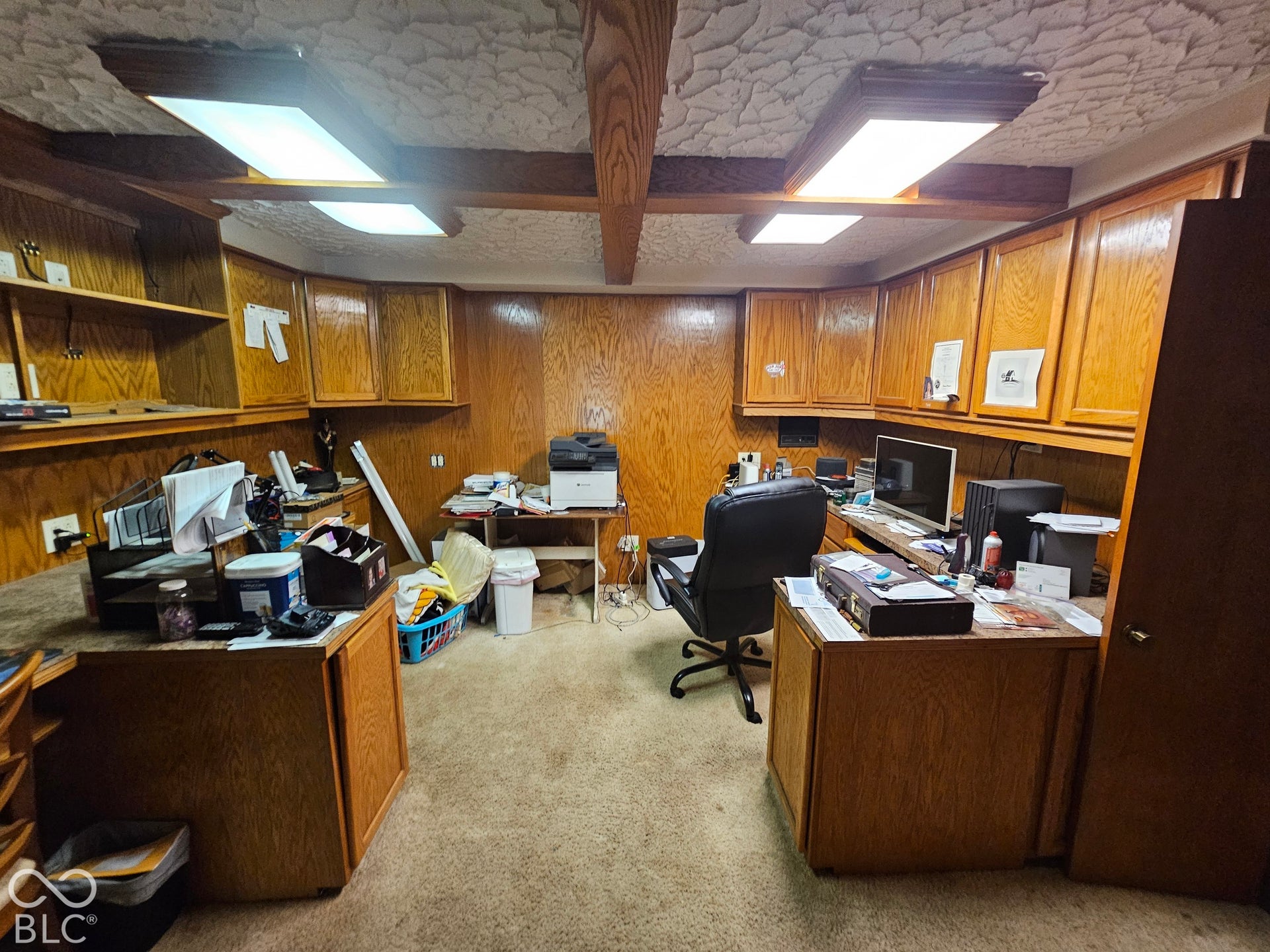Wood-paneled walls with extensive built-in cabinetry, textured ceiling, exposed wood beams, and flush-mount lighting fixtures