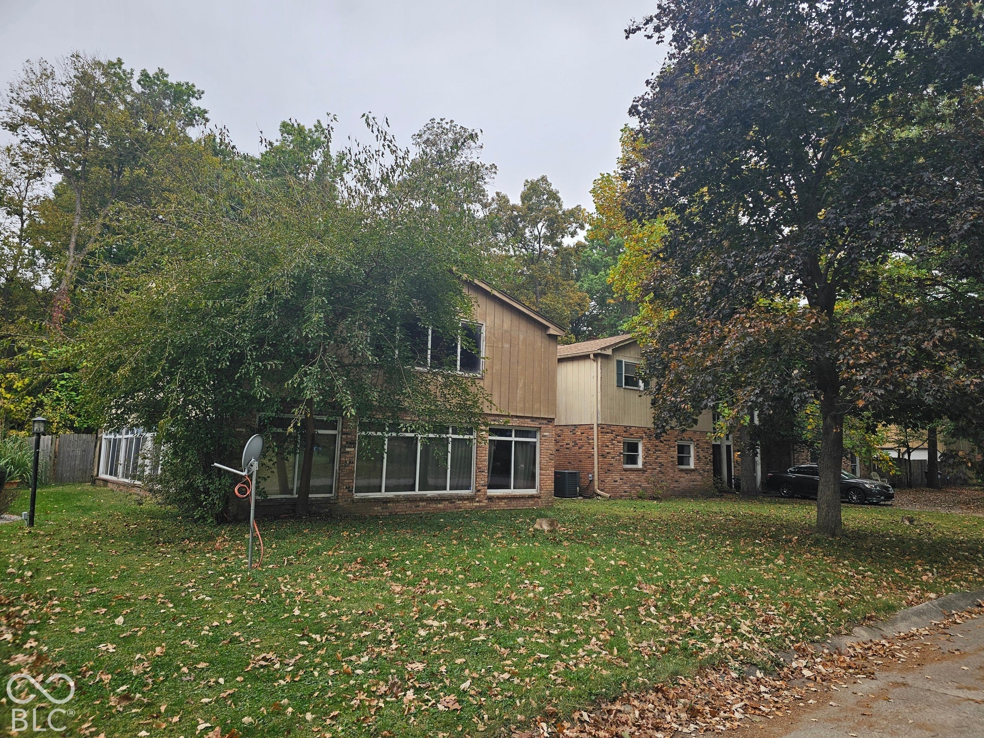 Split-level exterior featuring a brick and wood-paneled facade, large multi-pane windows, and a mature treed lot