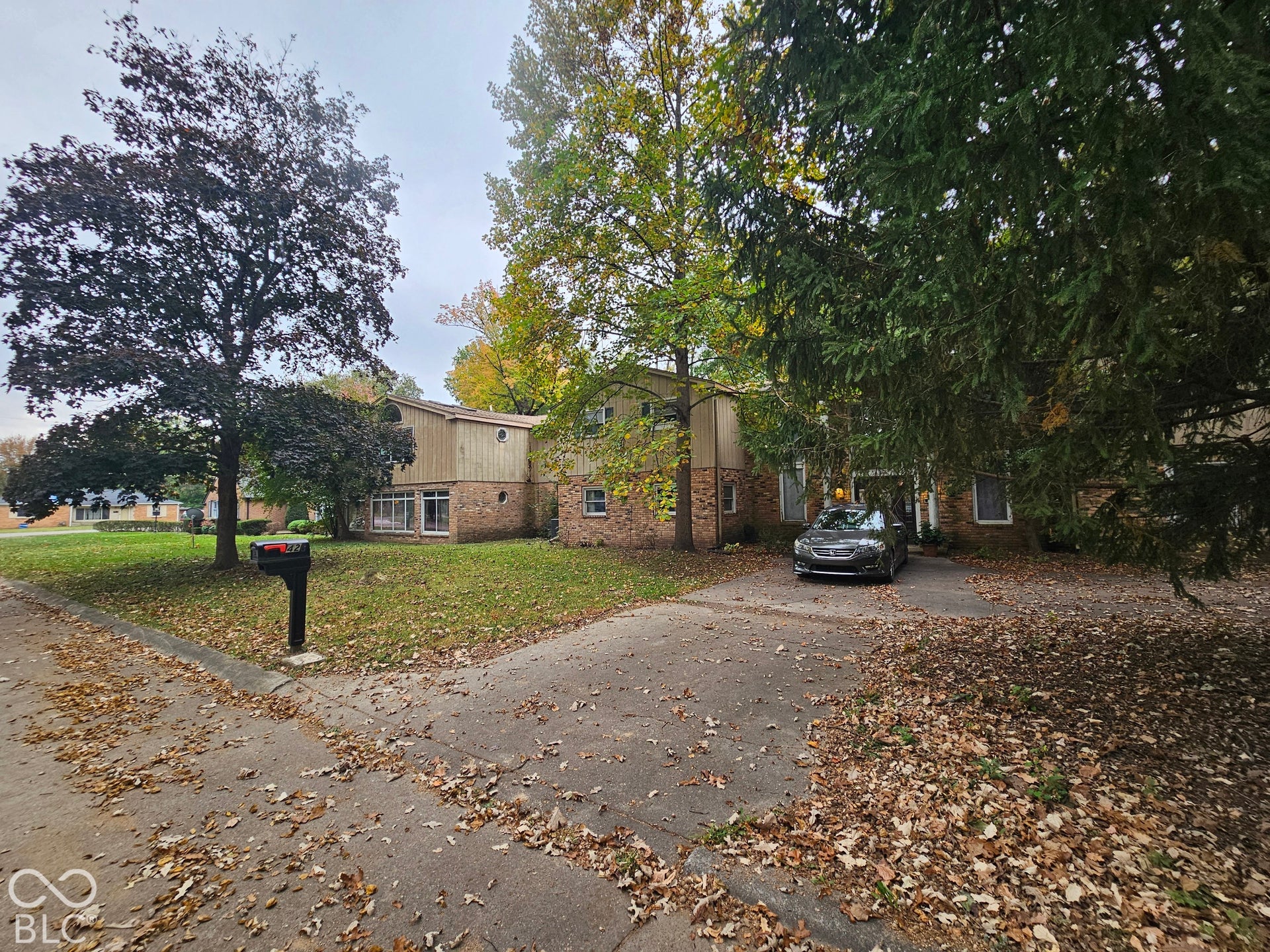 Multi-level exterior featuring a brick and vertical wood-finish facade, expansive front lawn, paved driveway, and mature trees