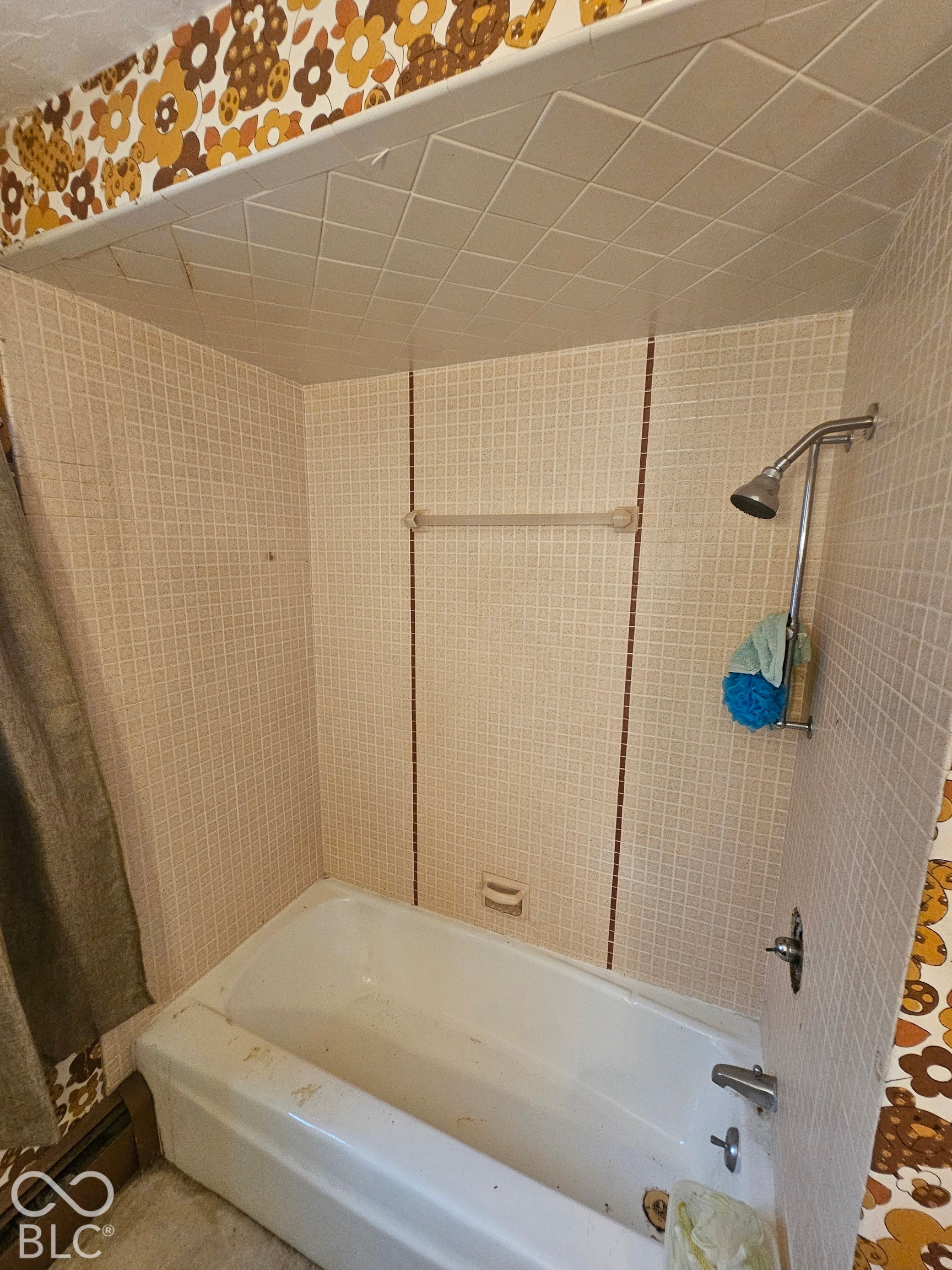 Recessed bathtub enclosure featuring a tiled surround with decorative linear accents, a mounted shower head, and patterned wall covering