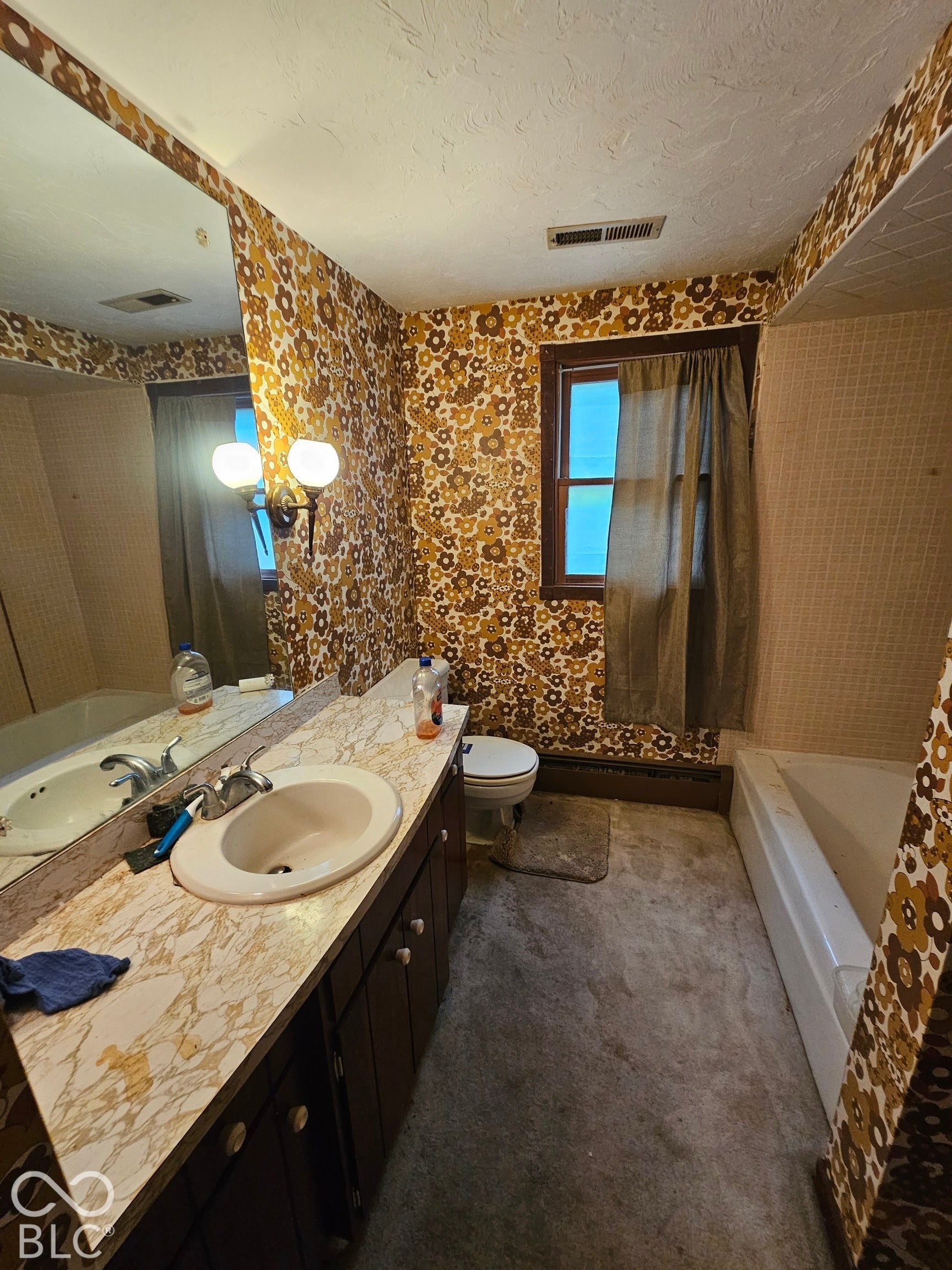 Bathroom featuring a laminate vanity countertop with an integrated oval basin, dual-light wall fixture, large wall-mounted mirror, and an enclosed soaking tub