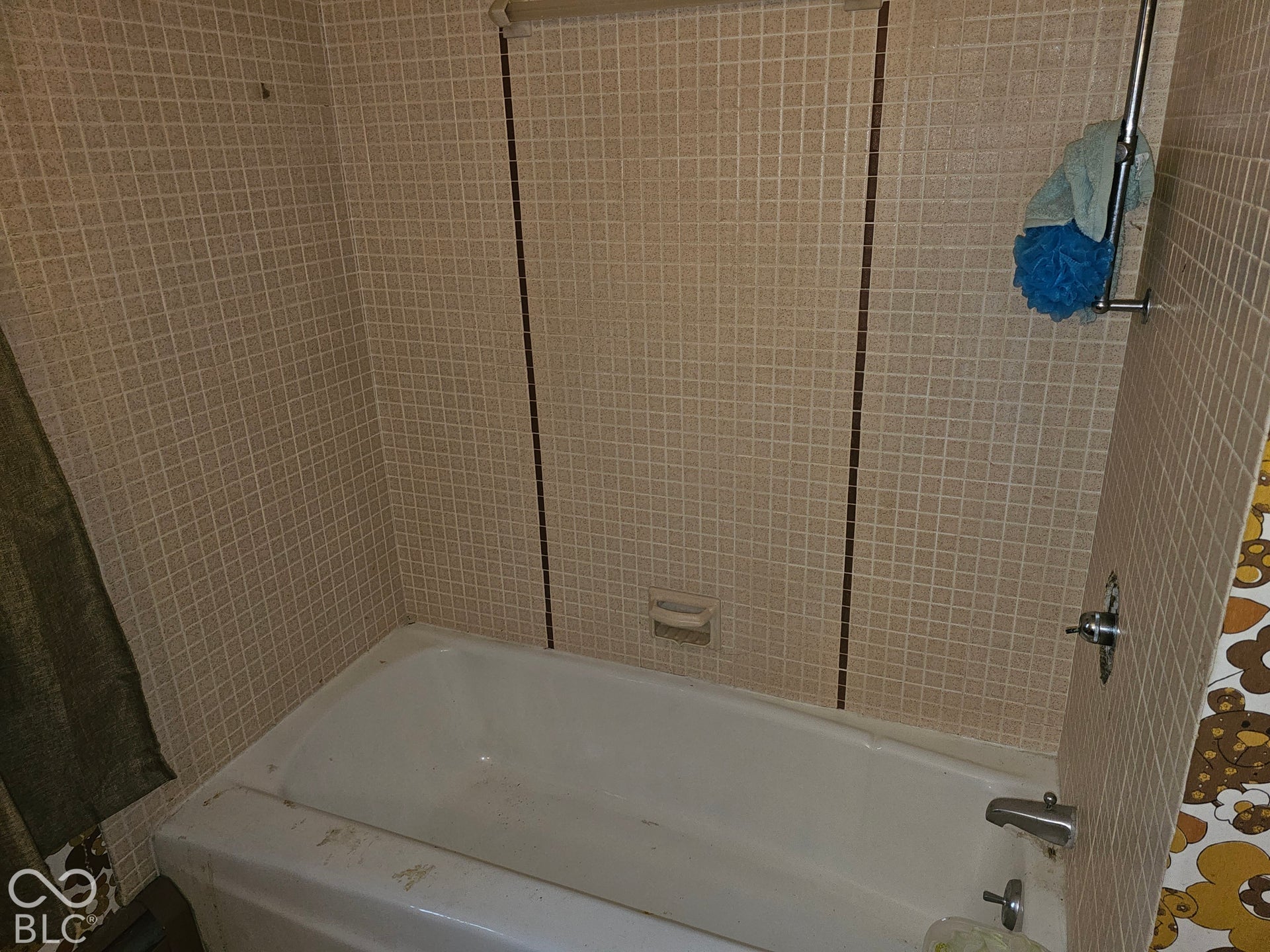 Bathtub surround featuring grid-patterned ceramic tile, vertical decorative accent tiling, integrated soap dish, and chrome-finish hardware