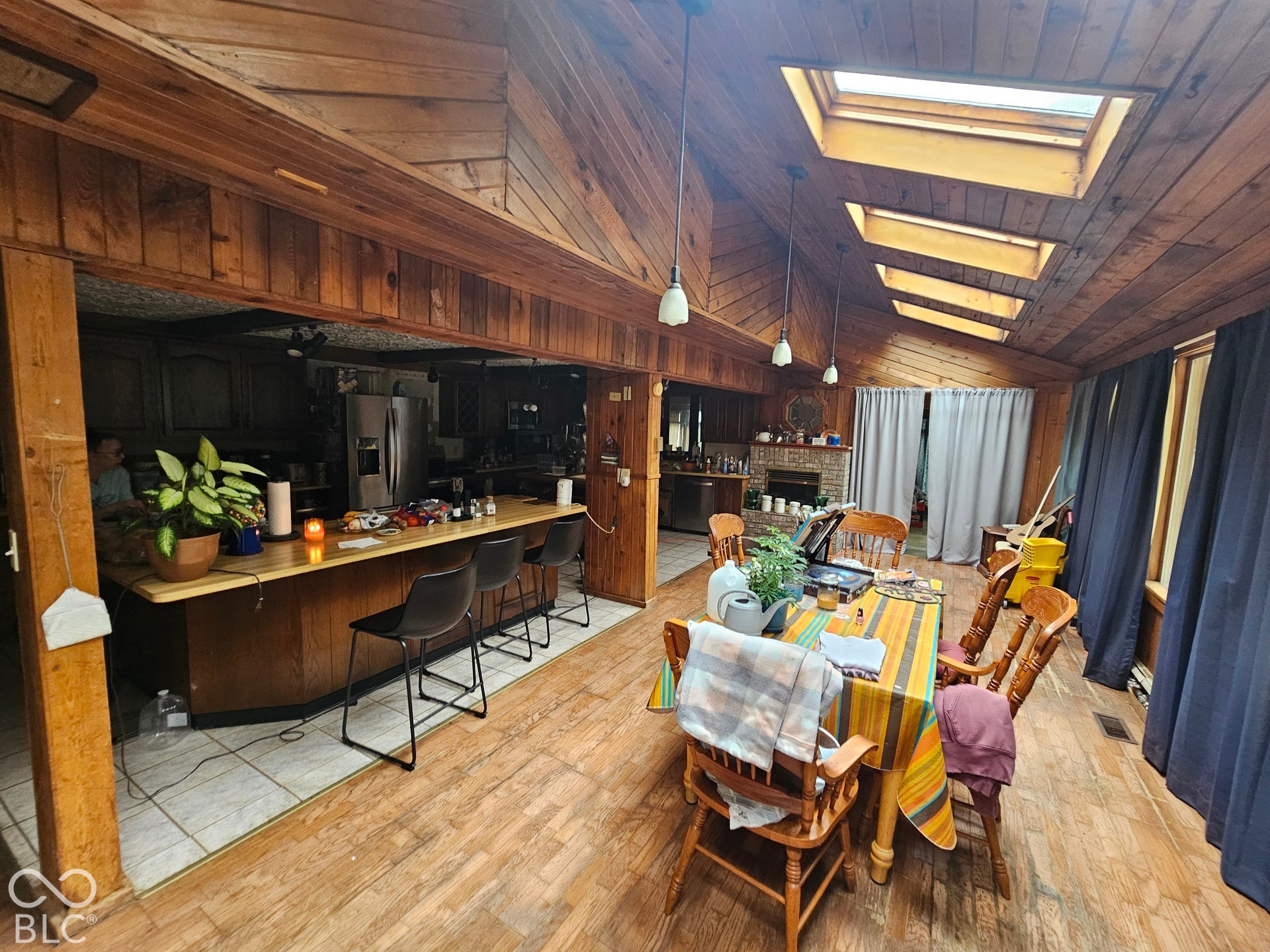 Vaulted wood-paneled ceiling with skylights, wood-finish flooring, and a stone-surround fireplace