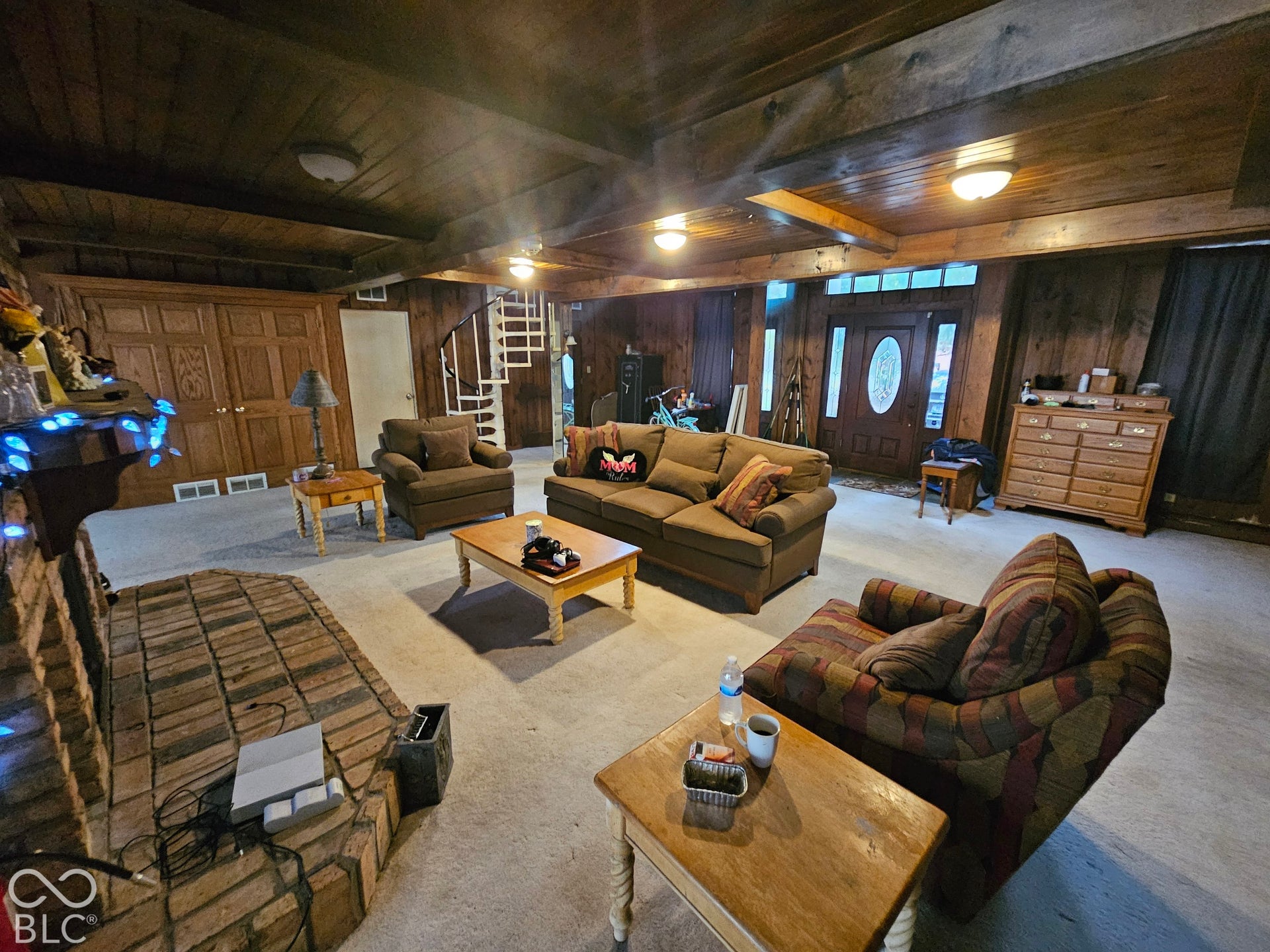 Living space featuring exposed wood-beam ceilings, paneled wood walls, a masonry fireplace, and a white spiral staircase