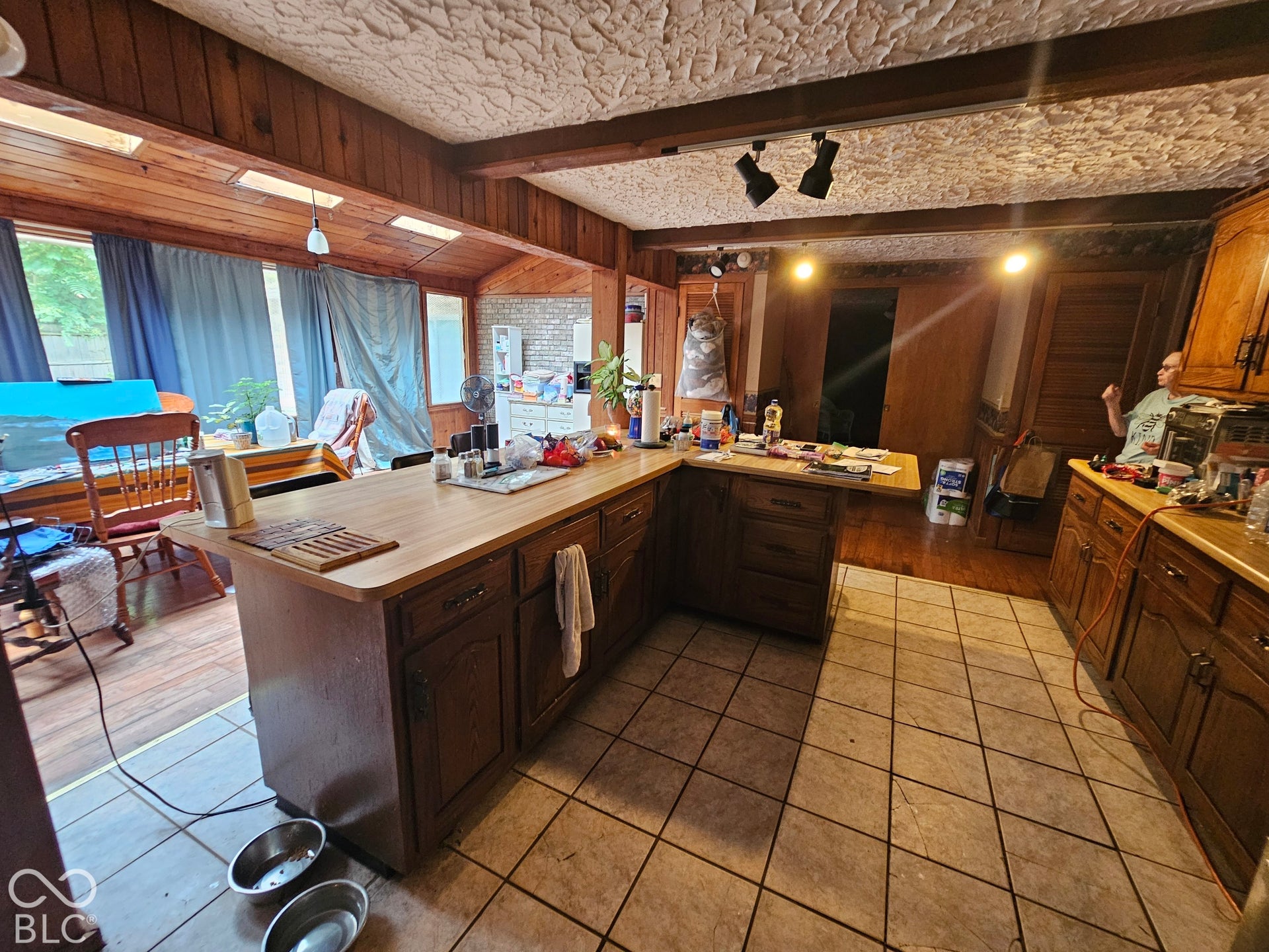 Kitchen featuring wood cabinetry, a wrap-around breakfast bar, ceramic tile flooring, exposed wood ceiling beams, and wood-paneled walls