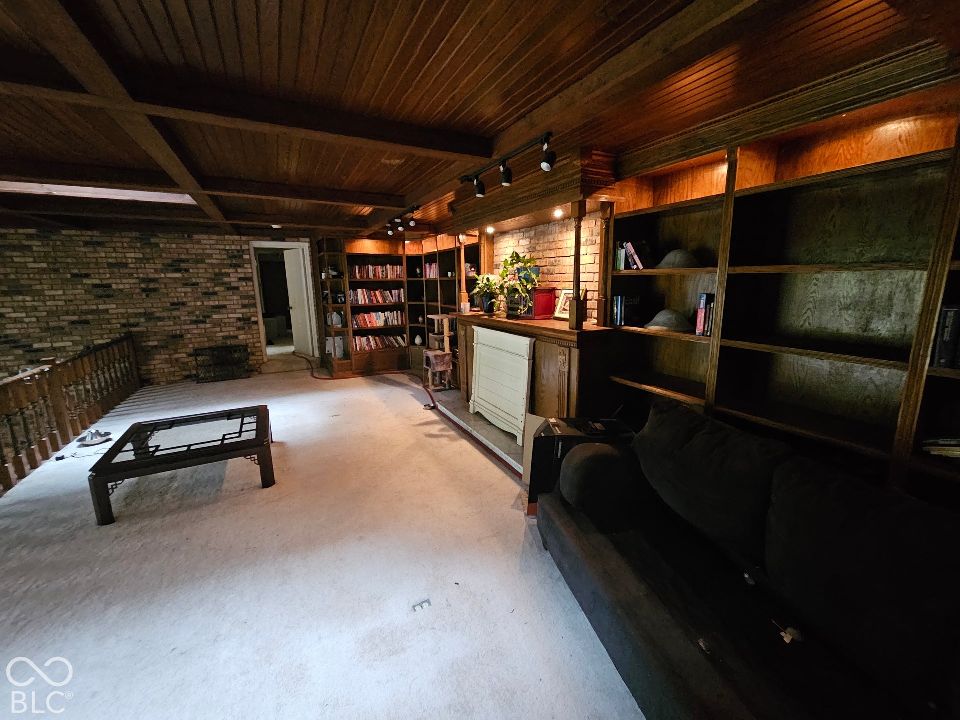 Wood-beamed ceiling with beadboard paneling, floor-to-ceiling built-in wood shelving, exposed brick masonry wall, and wooden balustrade