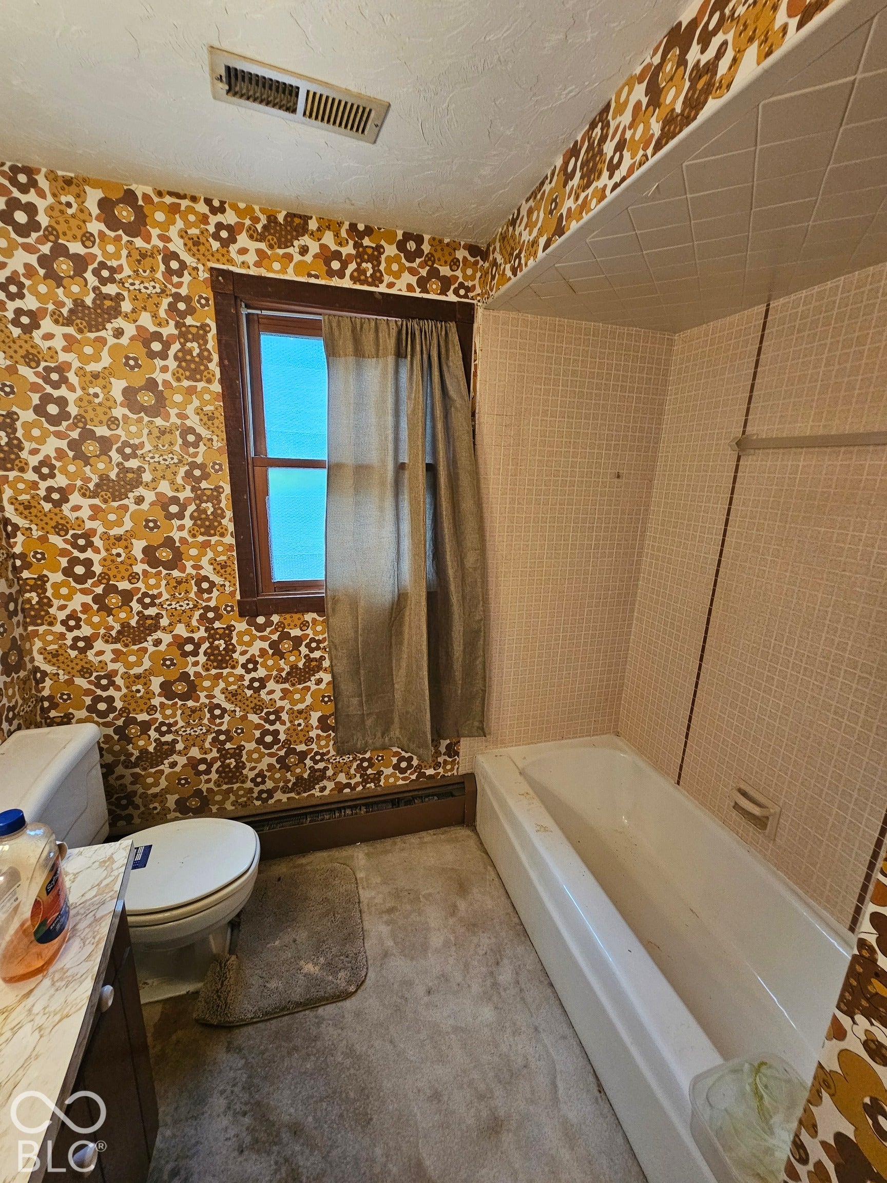 Bathroom featuring a shower and tub combination with tiled surround, wood-trimmed window, and patterned wall covering