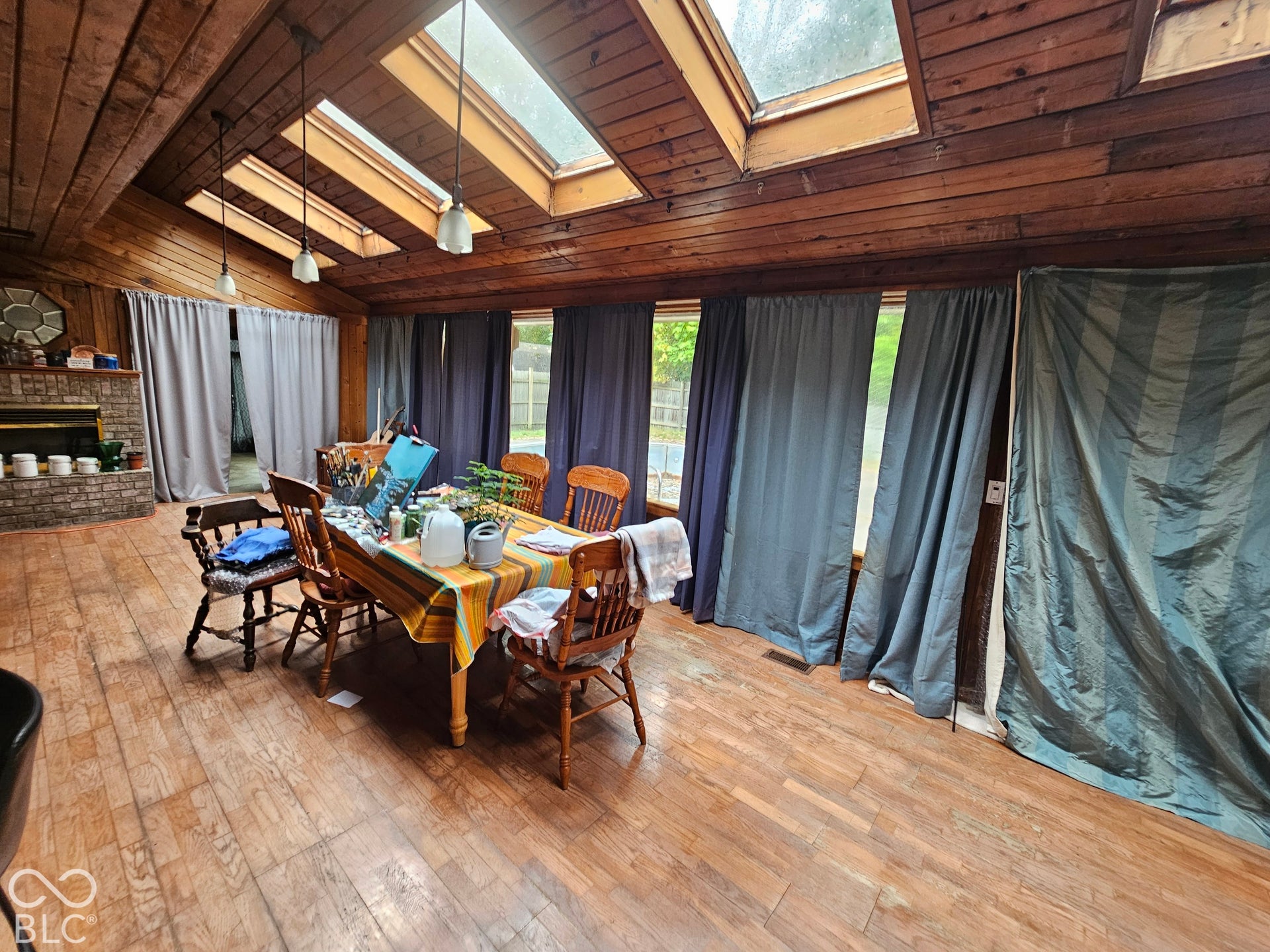 Spacious interior featuring wood-paneled walls and ceilings, three skylights, wood-finish flooring, and a brick fireplace