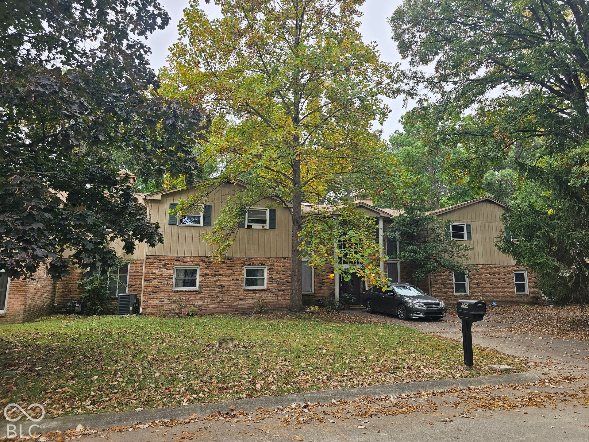 Two-story exterior featuring a brick and vertical wood-paneled facade, dark-framed shutter accents, and a paved driveway