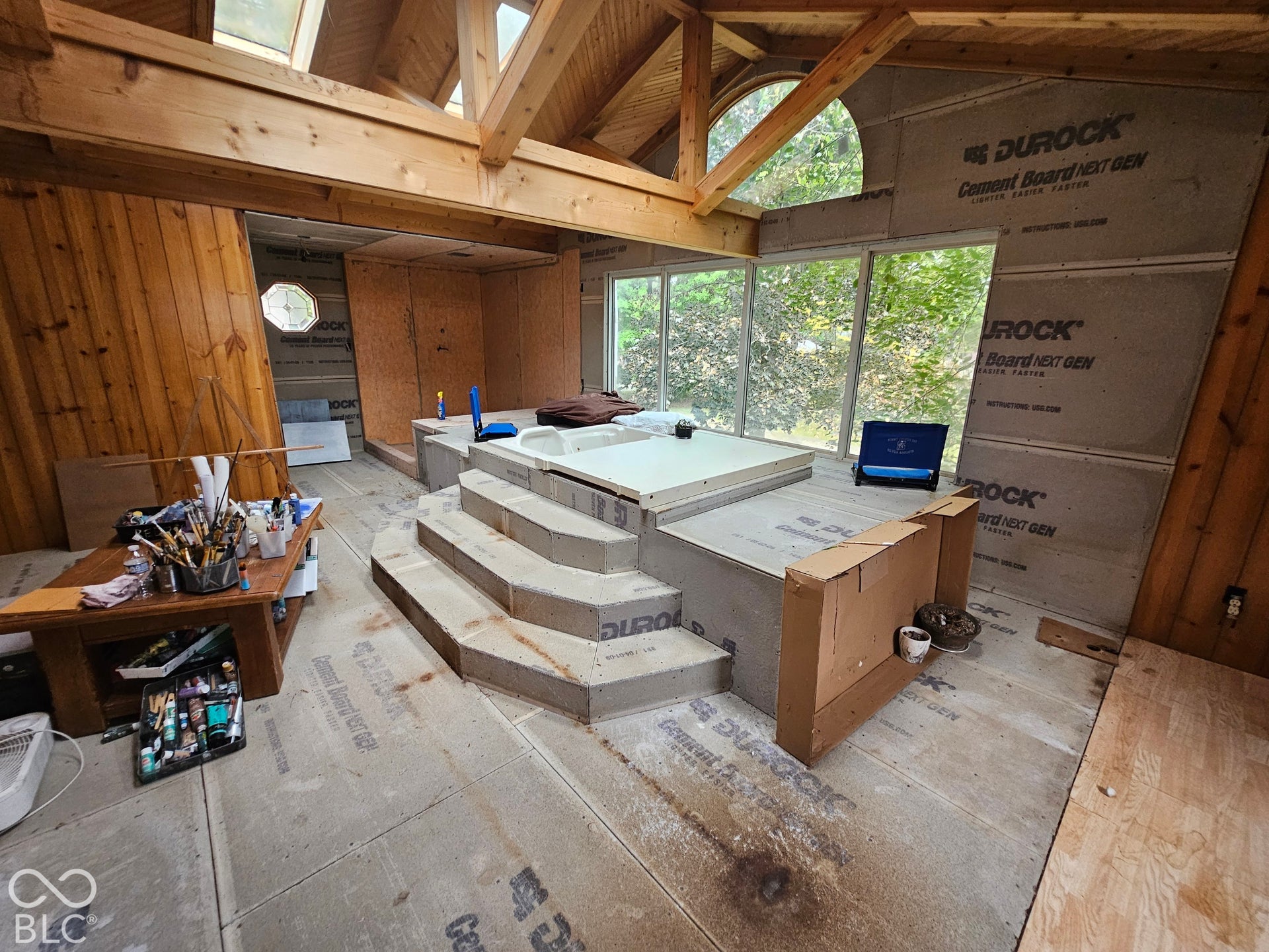 Vaulted wood-beamed ceiling with exposed trusses, large arched window, multiple skylights, and a tiered platform structure featuring a recessed soaking tub
