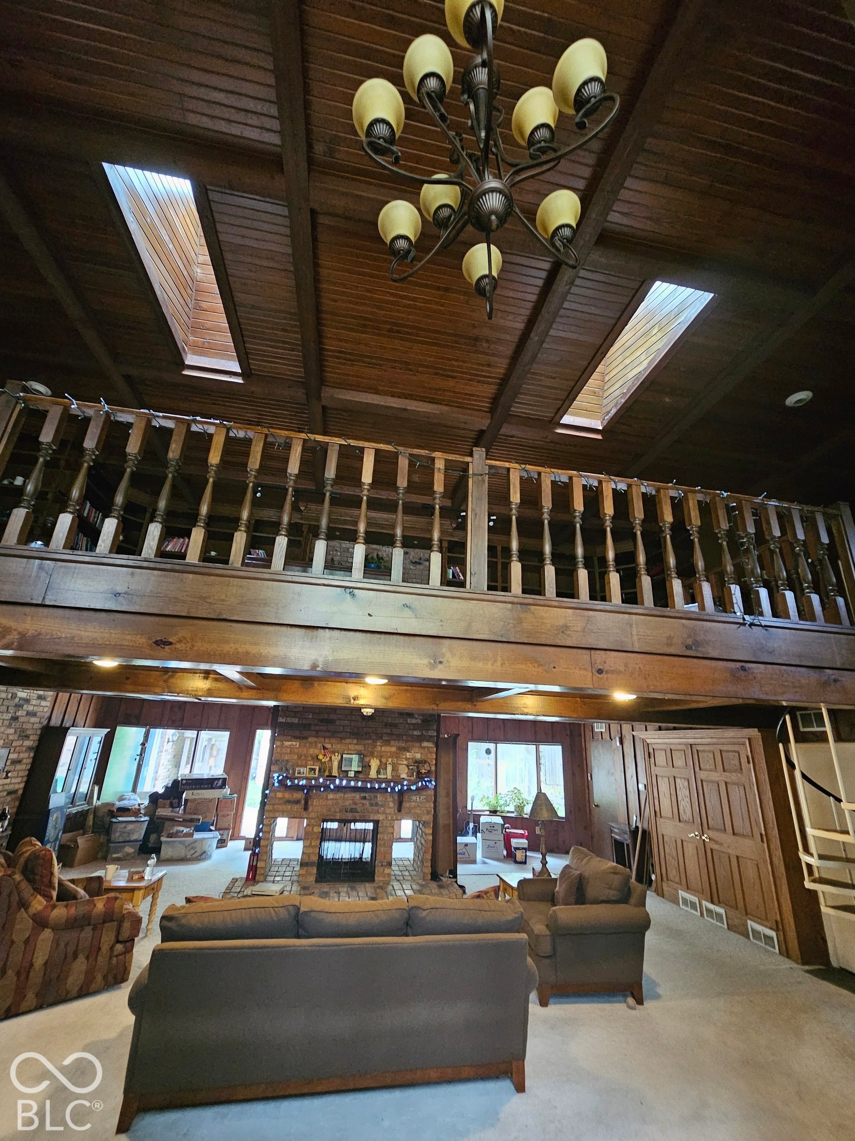 Vaulted wood-paneled ceiling with skylights, exposed timber beams, brick fireplace, and an elevated wood balustrade