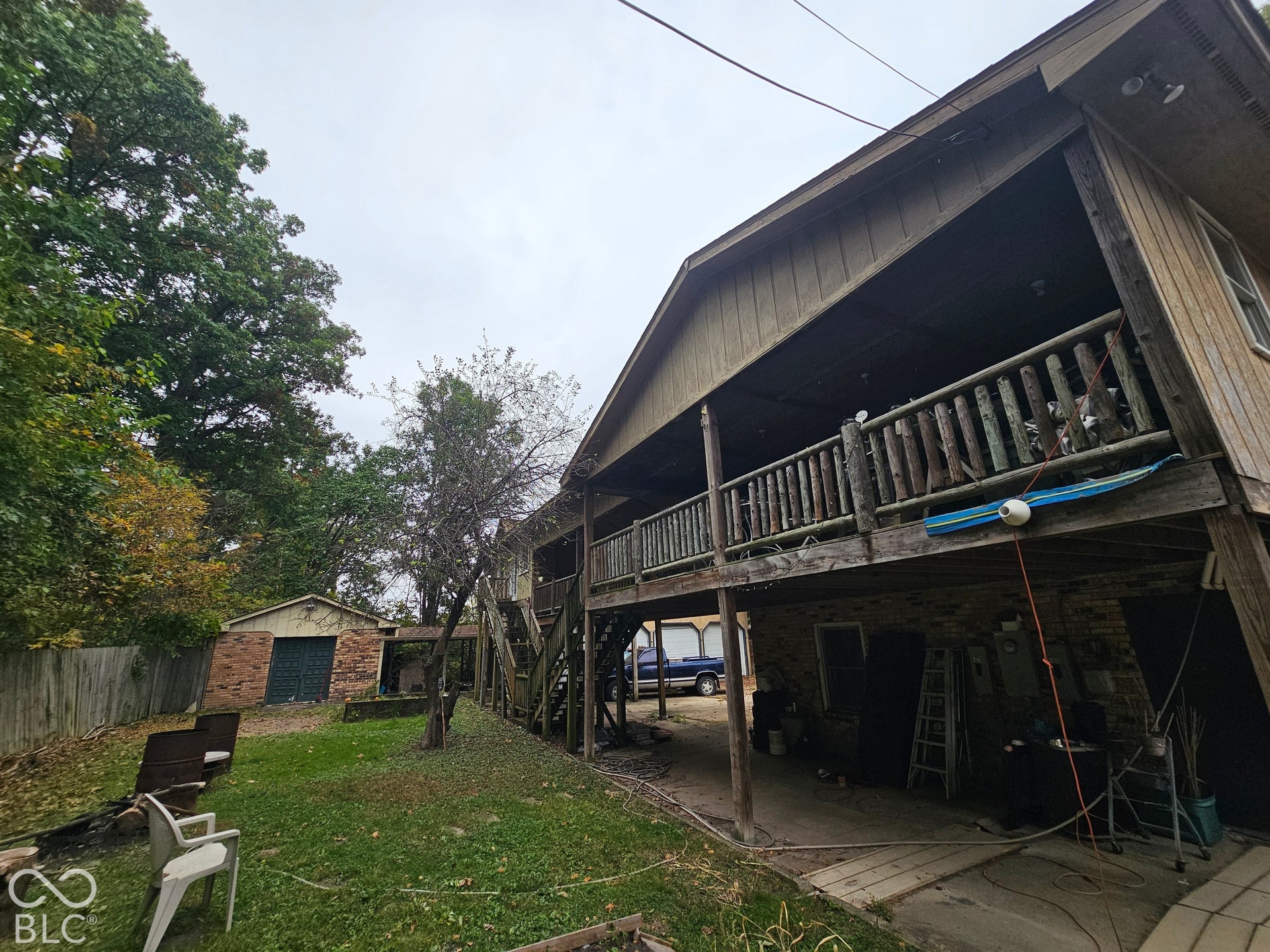 Exterior featuring a elevated wood deck with rustic railing, vertical wood siding, a concrete lower-level patio, and a detached brick storage structure