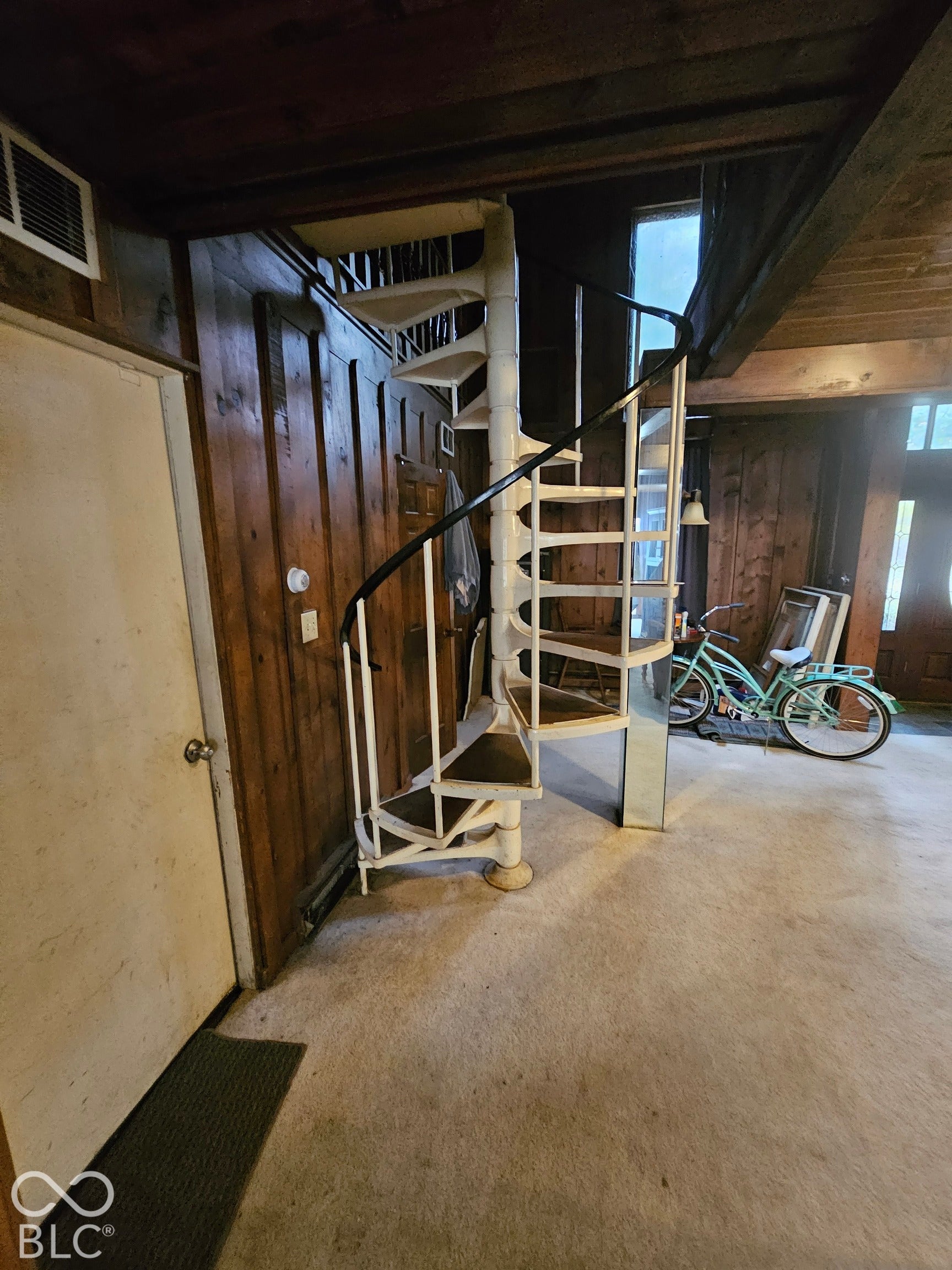 Spiral staircase featuring white metal framing, dark treads, and a black handrail, set against wood-paneled walls