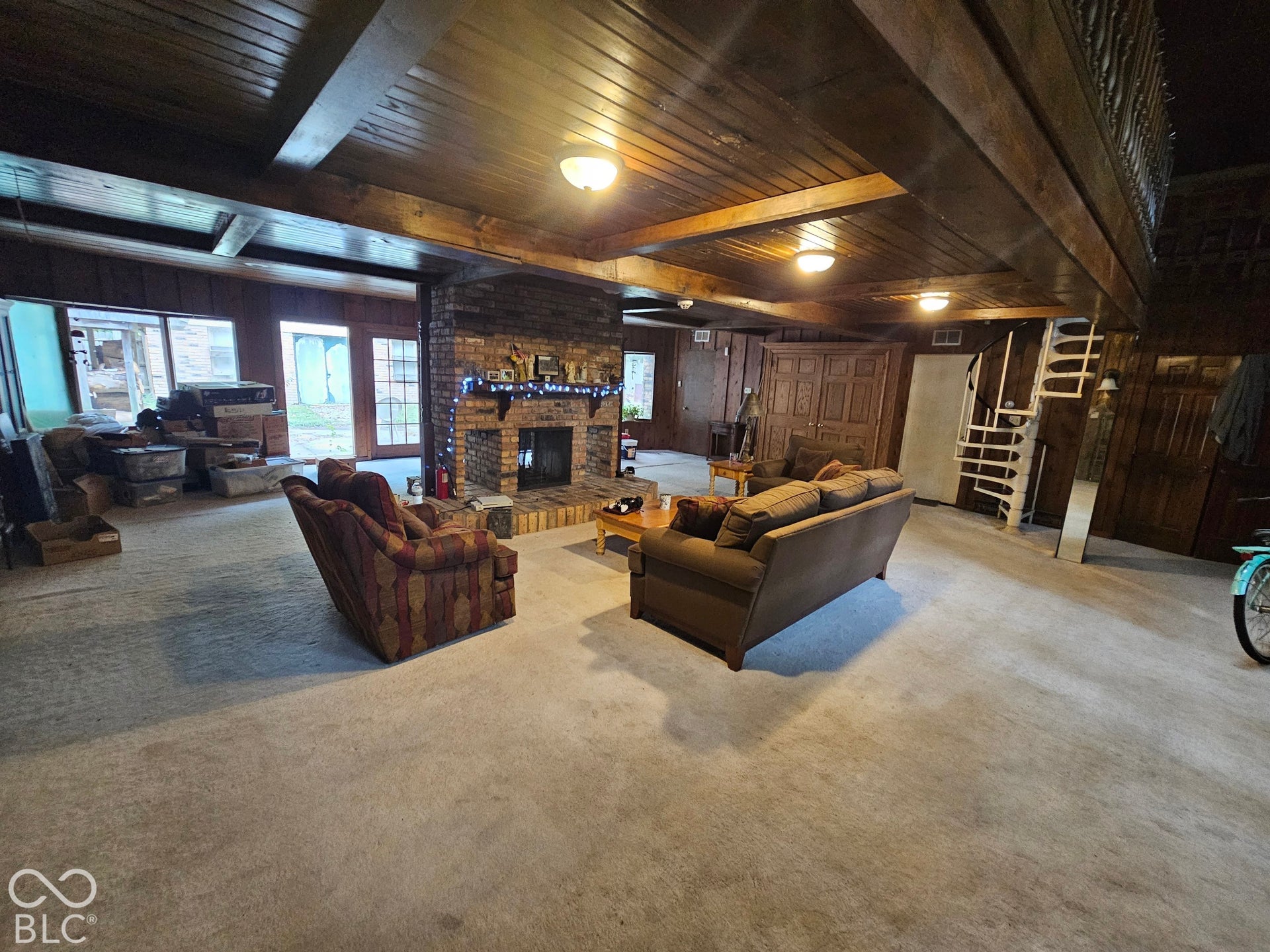 Exposed wood-beam ceiling, masonry fireplace with a wood mantel, spiral staircase, and wood-paneled walls