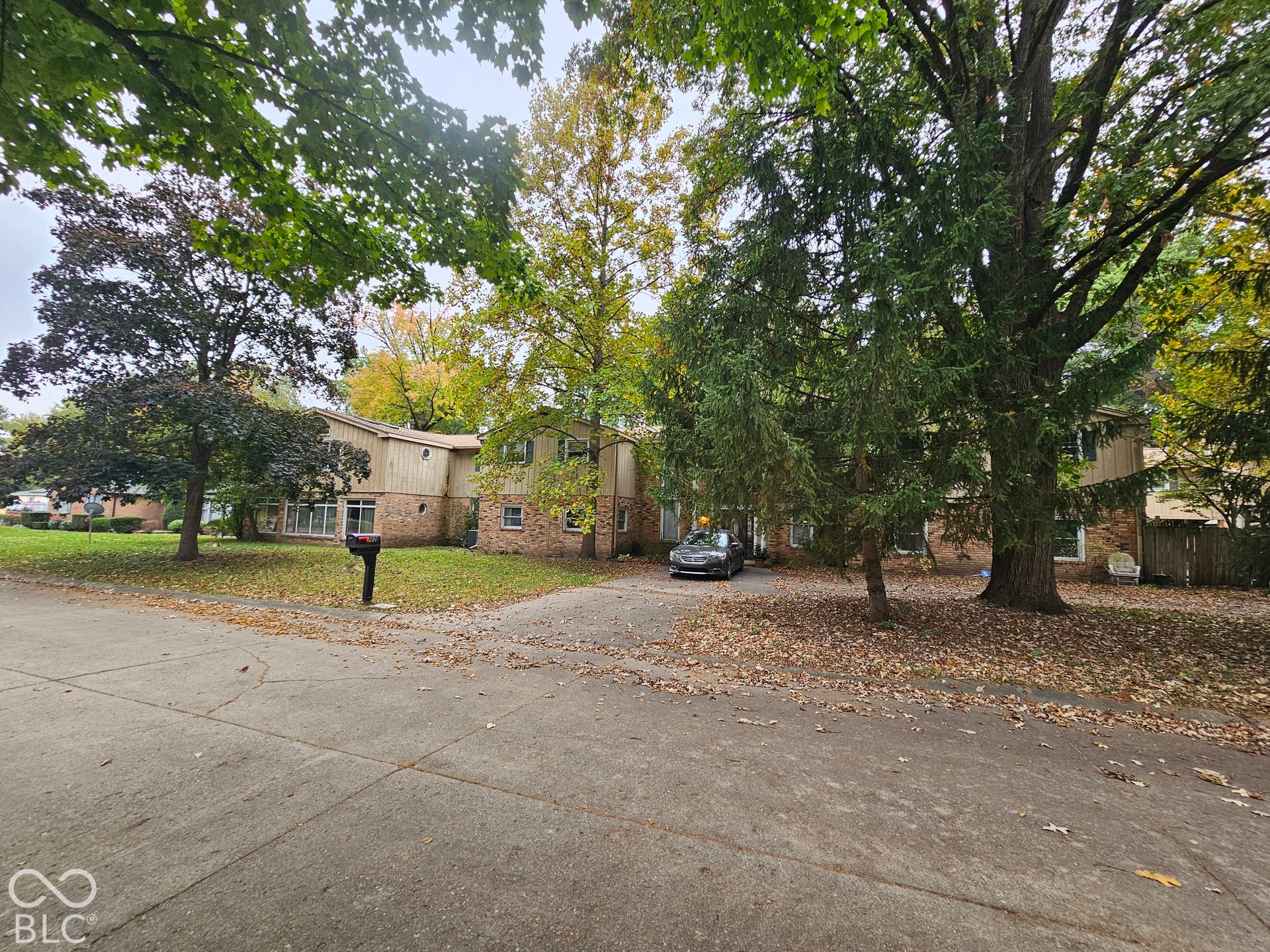 Multi-level exterior featuring a brick and siding facade, concrete driveway, and mature trees on a lot with grass coverage