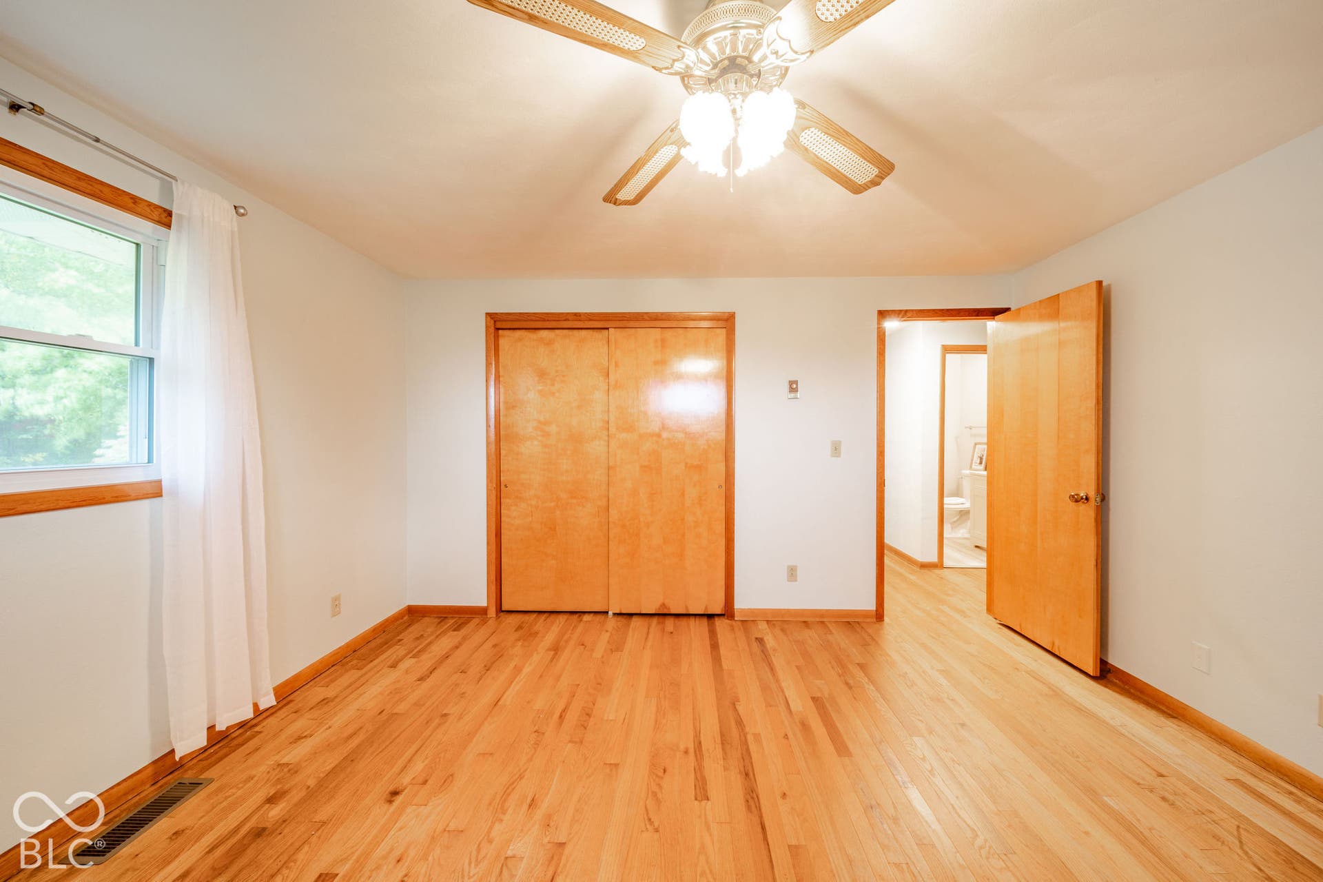 Wood-finish flooring, light wood-toned doors, dual-sliding closet doors, and a ceiling-mounted light fixture with a central fan