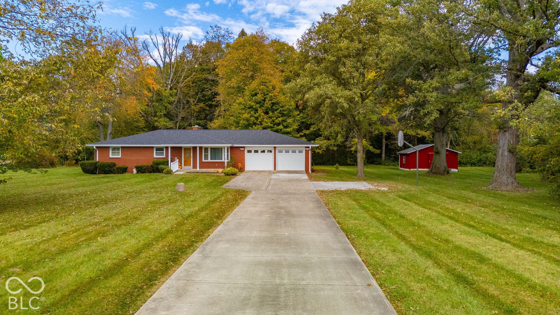 Single-story brick exterior featuring a multi-car garage, concrete driveway, and detached storage building situated on an expansive lot with mature trees