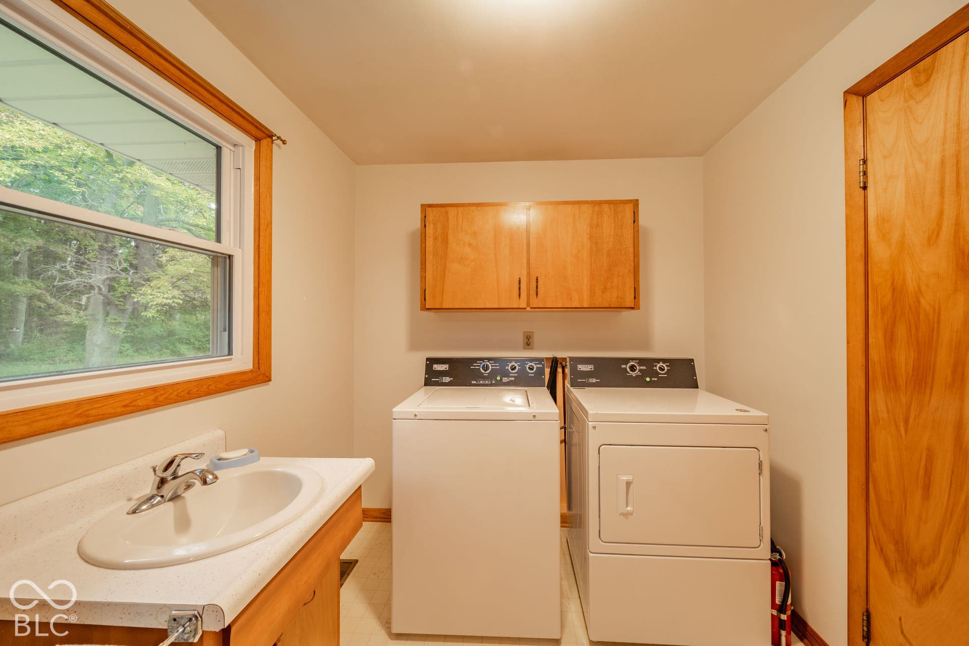 Laundry area featuring a drop-in sink, wood-finish cabinetry, a white countertop, and natural wood trim surrounding the window and doorway