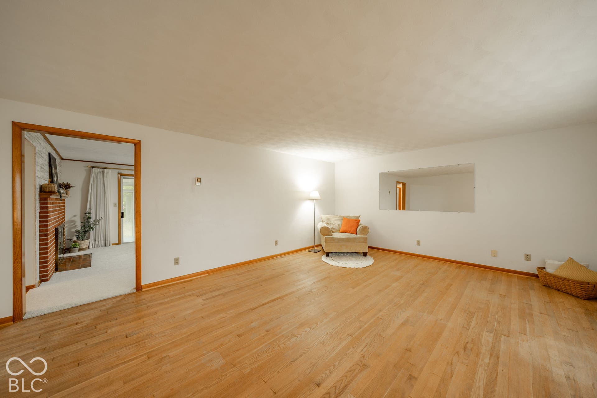 Interior space featuring wood-finish flooring, a wall-mounted rectangular mirror, and an exposed brick masonry fireplace
