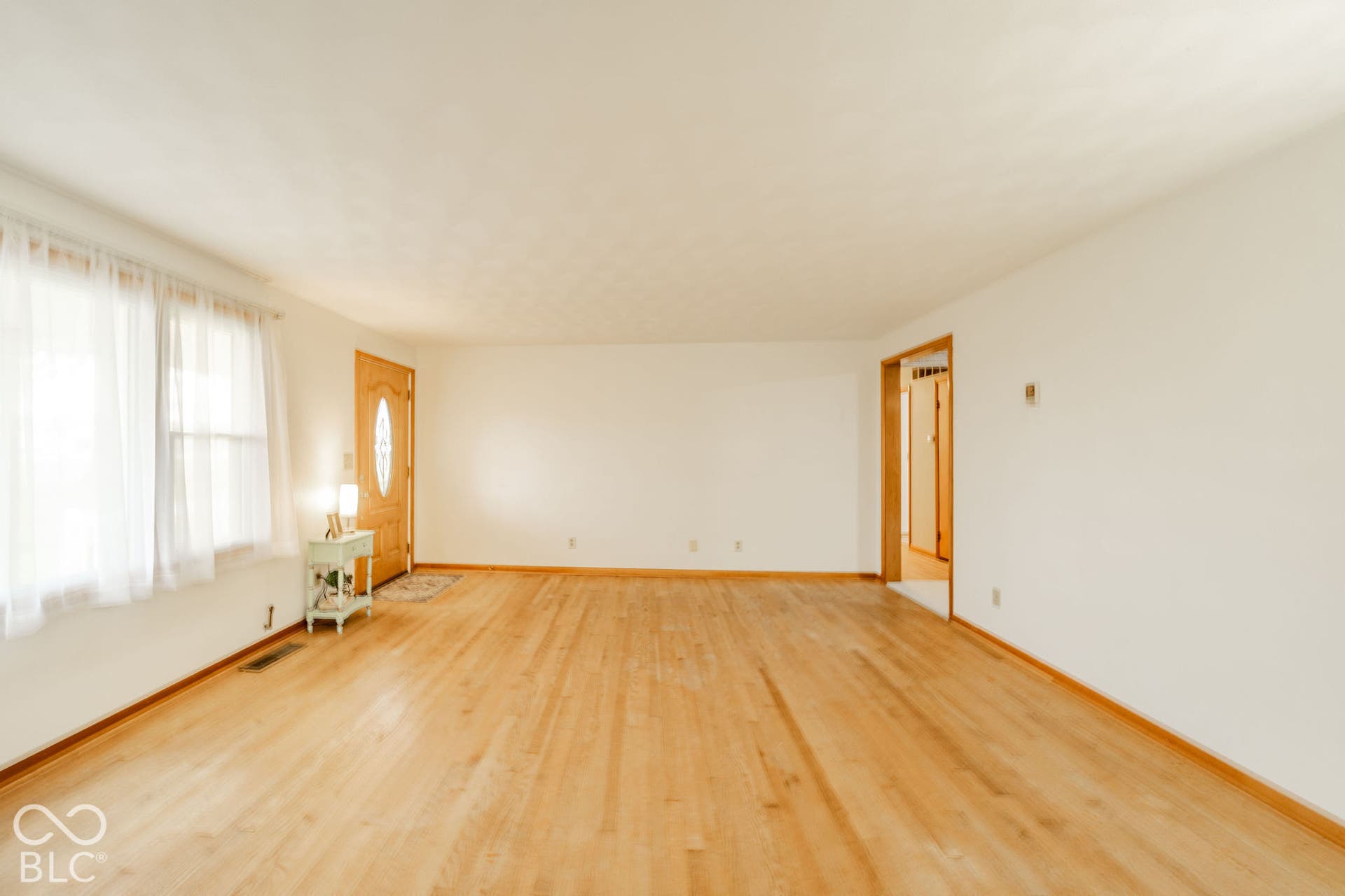 Spacious room featuring wood-finish flooring, neutral wall paint, and a solid wood front door with an oval glass insert