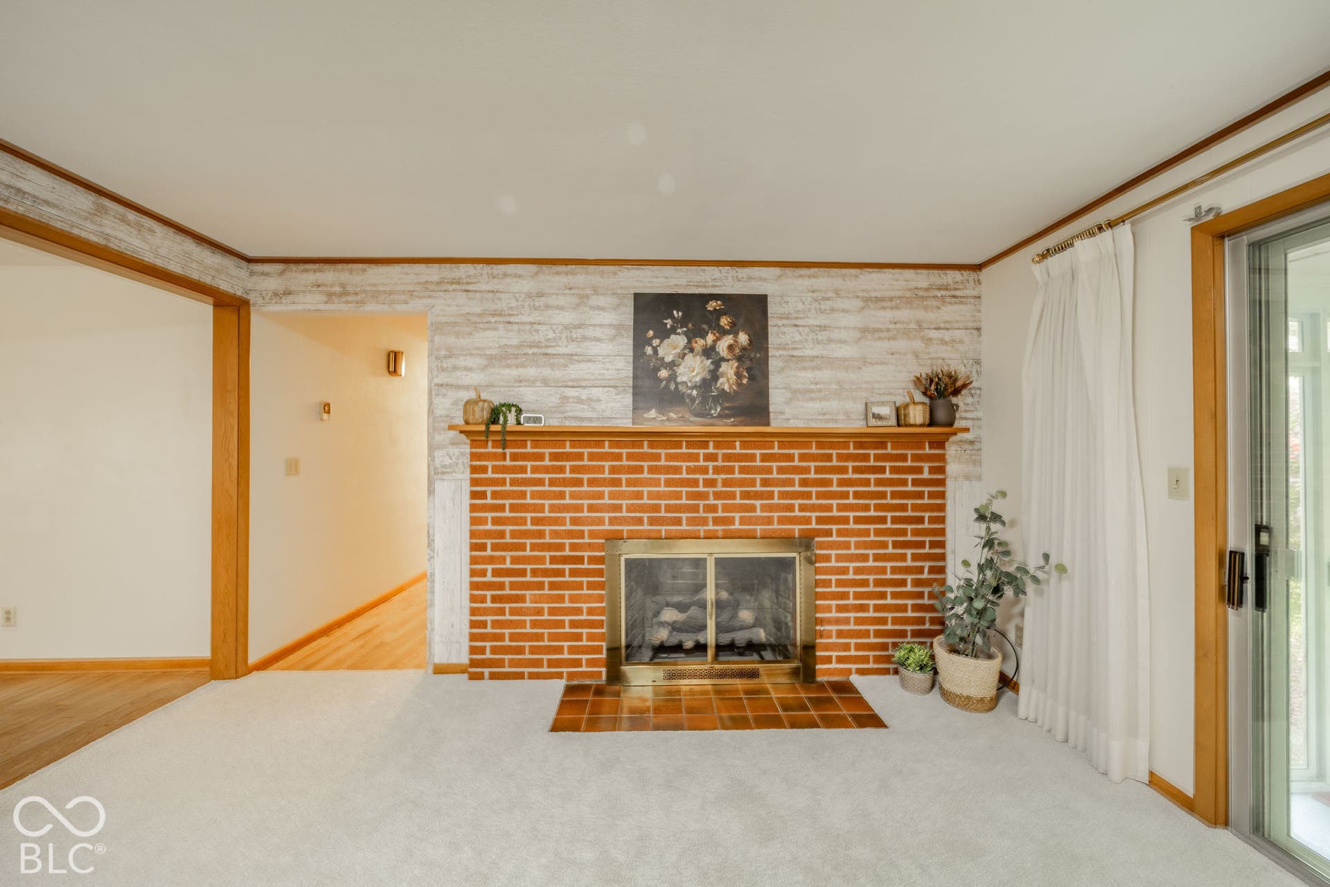 Fireplace featuring a red brick surround, wood mantel, metal hearth screen, and tile floor pad, accompanied by a textured accent wall