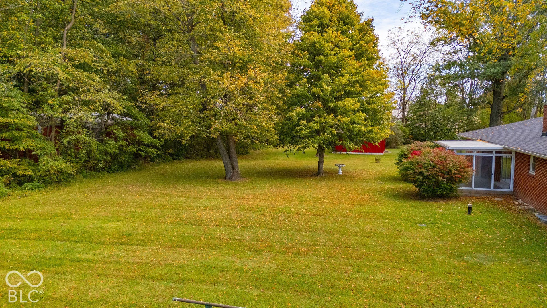 Expansive backyard featuring mature trees, a red exterior outbuilding, and an attached glass-enclosed patio with a red brick facade