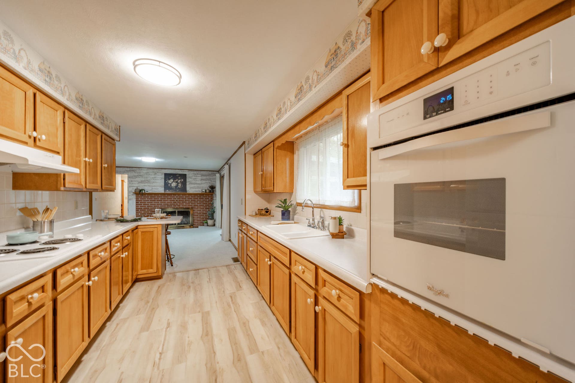 Kitchen featuring wood cabinetry, integrated white oven, solid-surface countertops, dual-basin sink, and wood-finish flooring