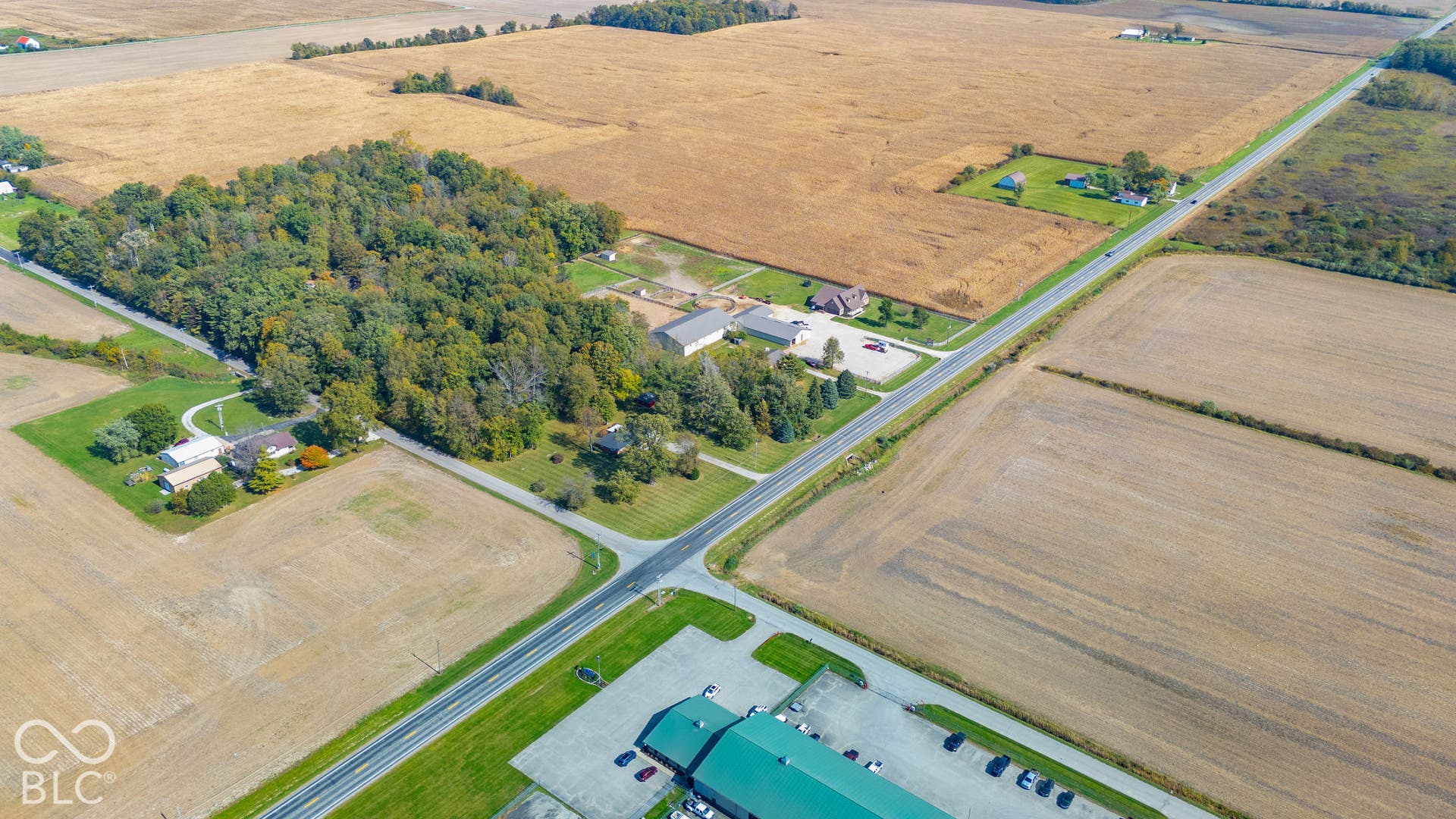 Aerial perspective of sprawling acreage featuring mature timber stands, expansive open fields, and paved road frontage