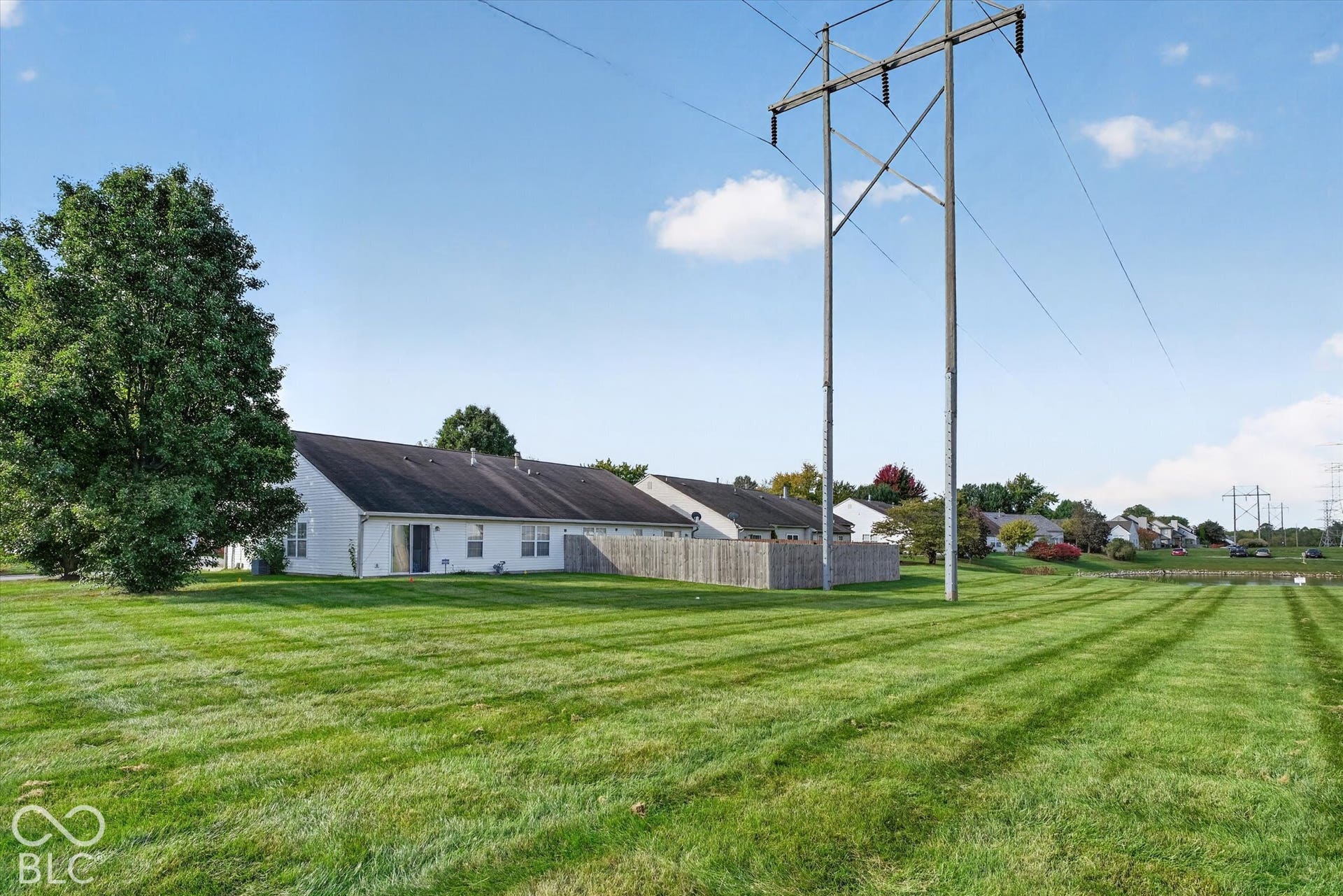Expansive green space featuring mature trees and a partial wood fence enclosure
