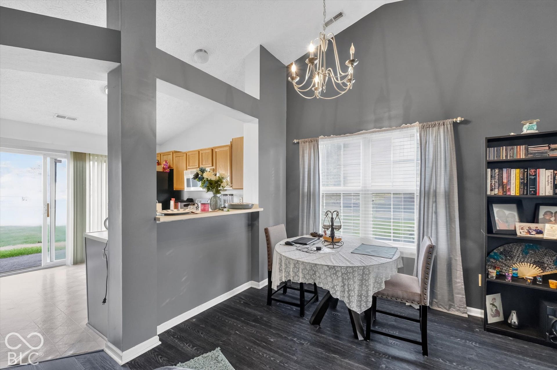 Vaulted ceiling featuring a multi-arm chandelier, wood-finish flooring, and a pass-through opening with a breakfast bar