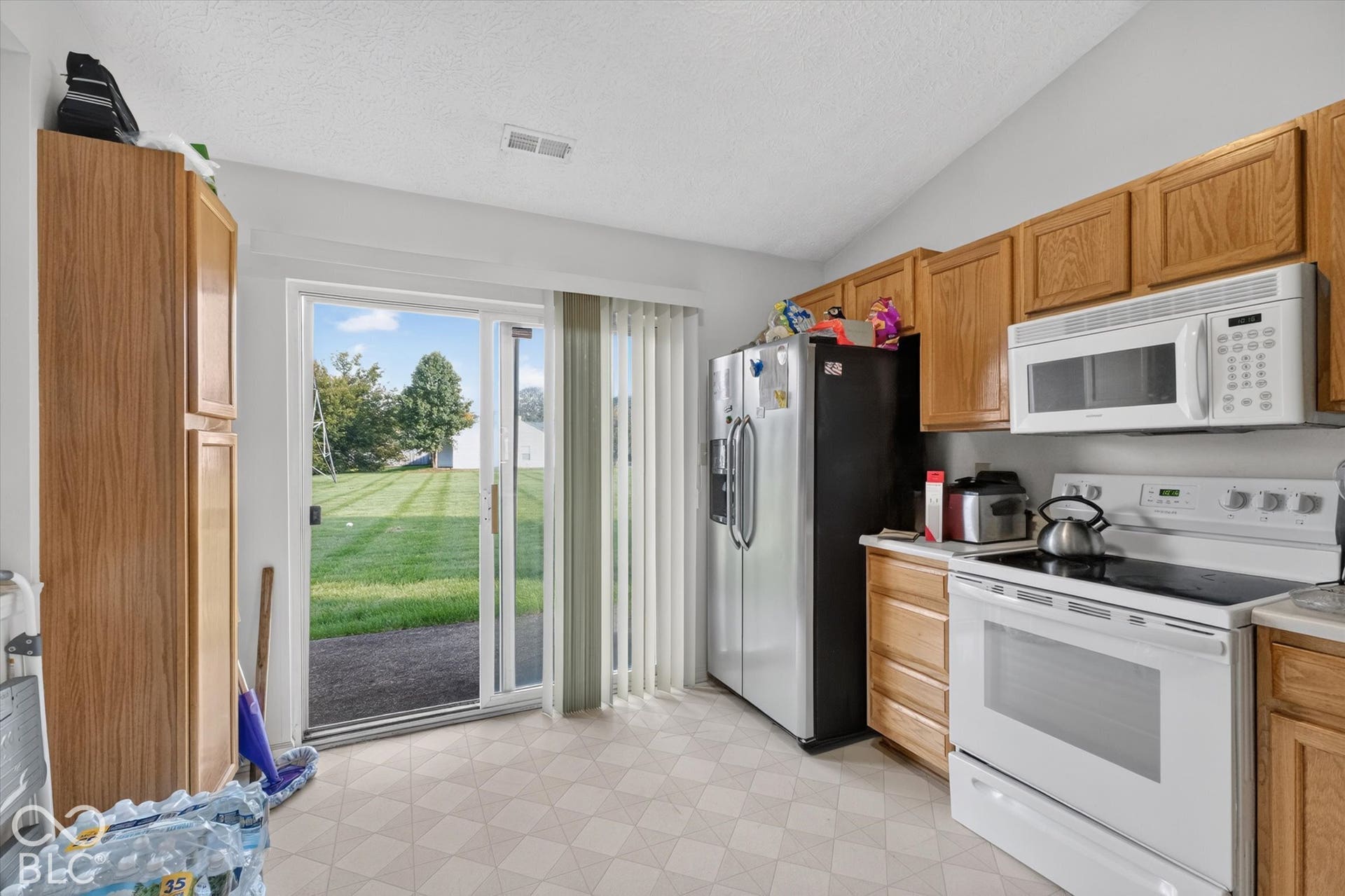 Kitchen featuring light-finish wood cabinetry, a sliding glass door, and a vaulted ceiling