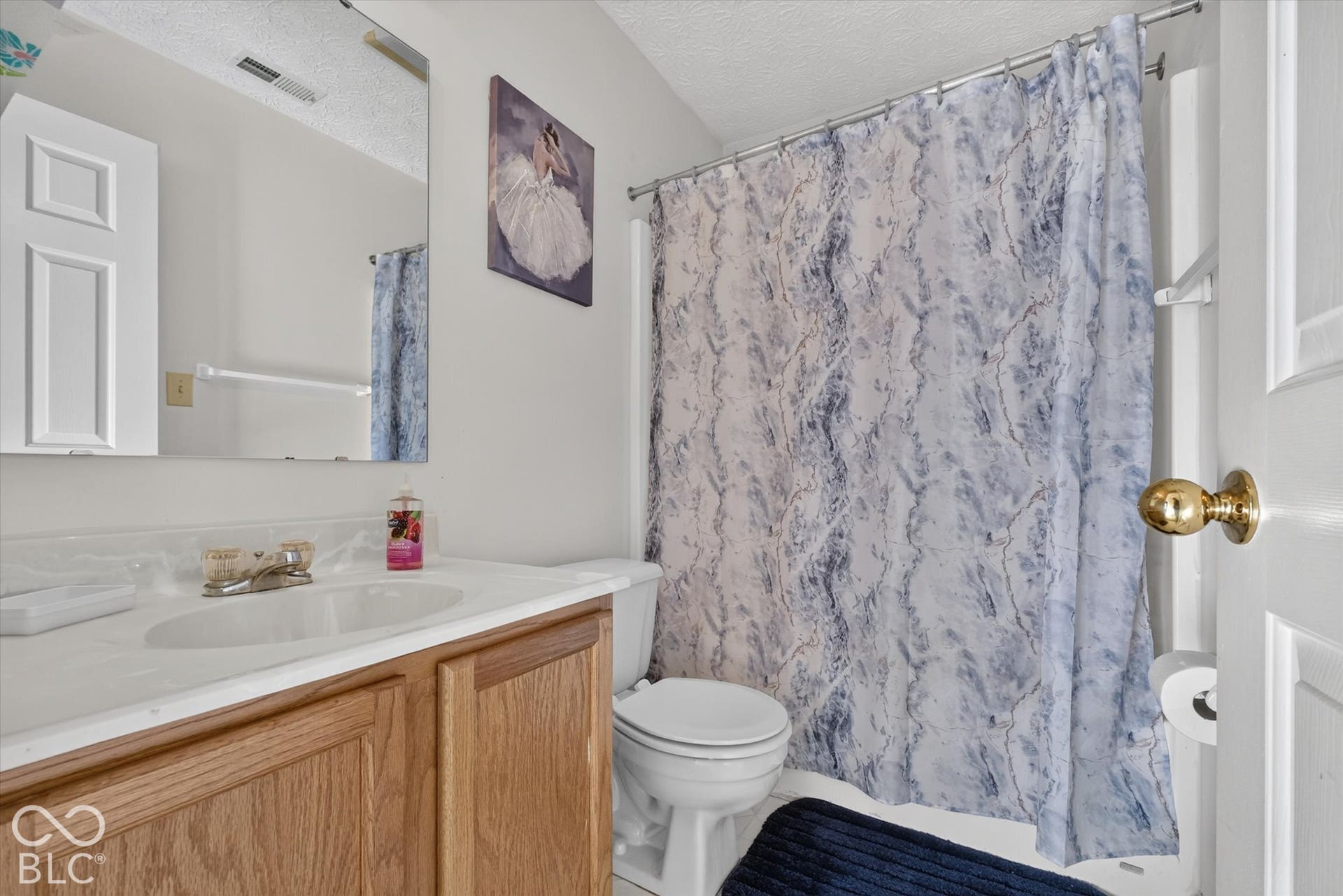 Full bathroom featuring a wood-finish vanity, integrated countertop with a circular basin, chrome faucet, wall-mounted mirror, and a tub-shower combination with a curtain rod