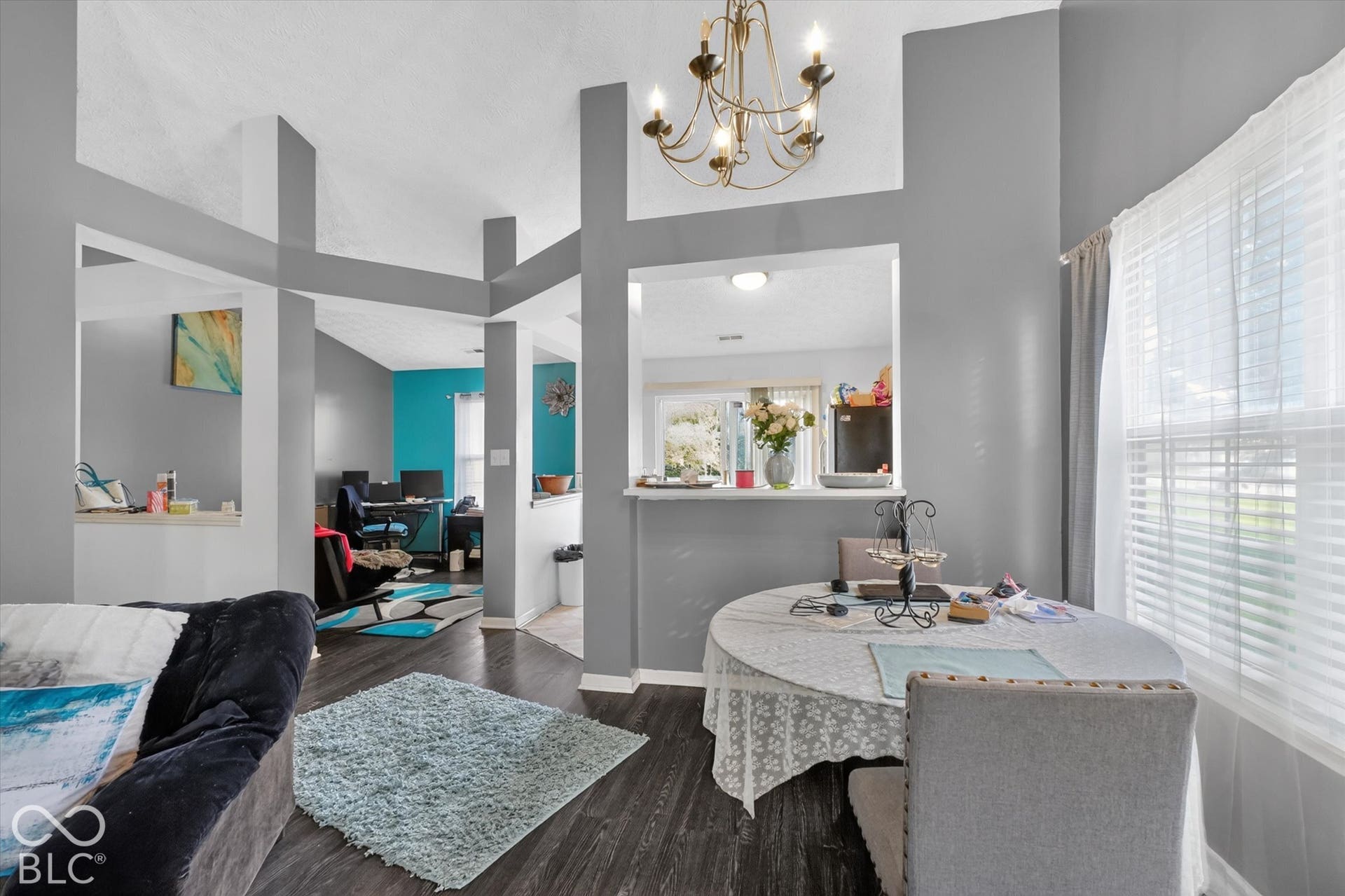 Vaulted ceilings featuring decorative architectural columns, dark wood-finish flooring, a multi-light chandelier, and a breakfast bar pass-through