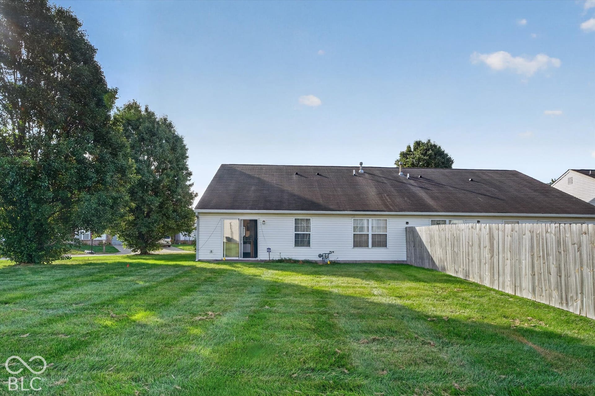 Expansive backyard featuring a large grass lawn, a wood privacy fence, and mature trees