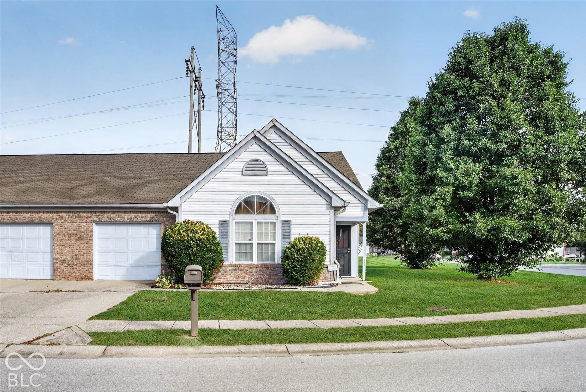Exterior featuring a combination of brick and horizontal siding, an arched window with decorative shutters, a concrete driveway, two attached garages, and mature landscaping