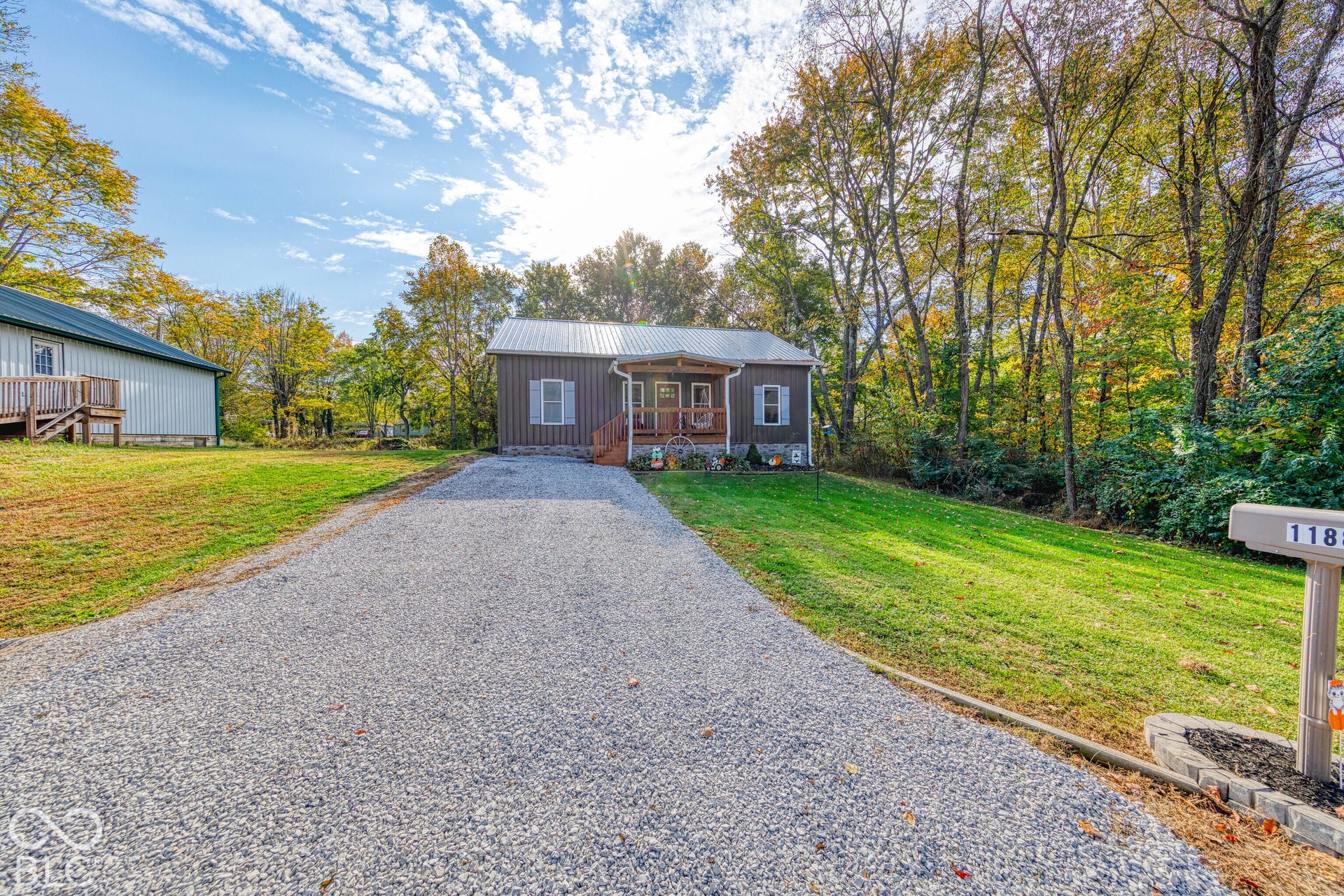 Single-story residence with a metal roof, front covered porch, stone veneer foundation, and a dedicated gravel driveway