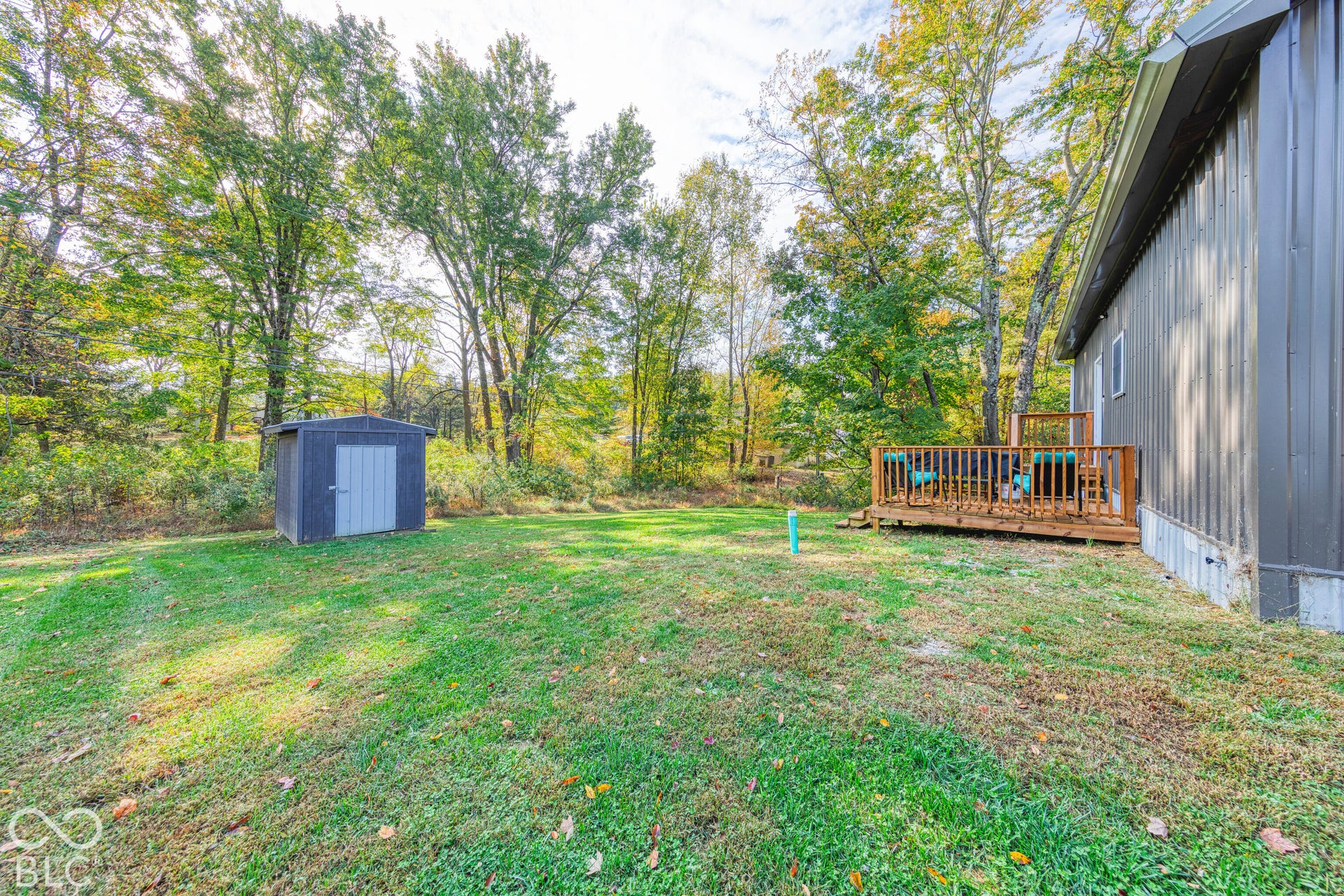 Backyard featuring a wood deck, detached storage shed, metal siding, and mature trees