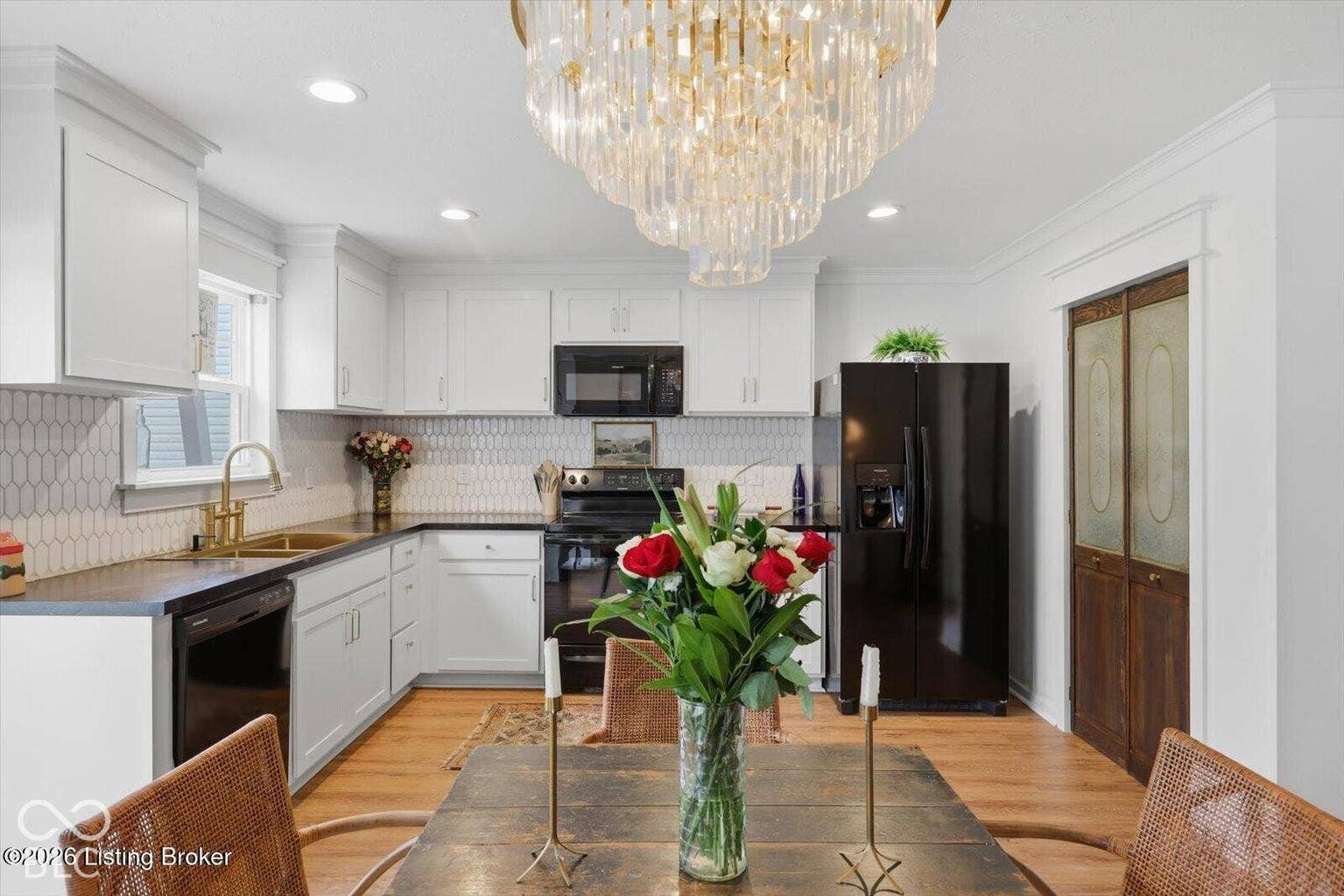 Kitchen featuring white cabinetry, hexagonal tile backsplash, dark countertops, wood-finish flooring, and a crystal chandelier