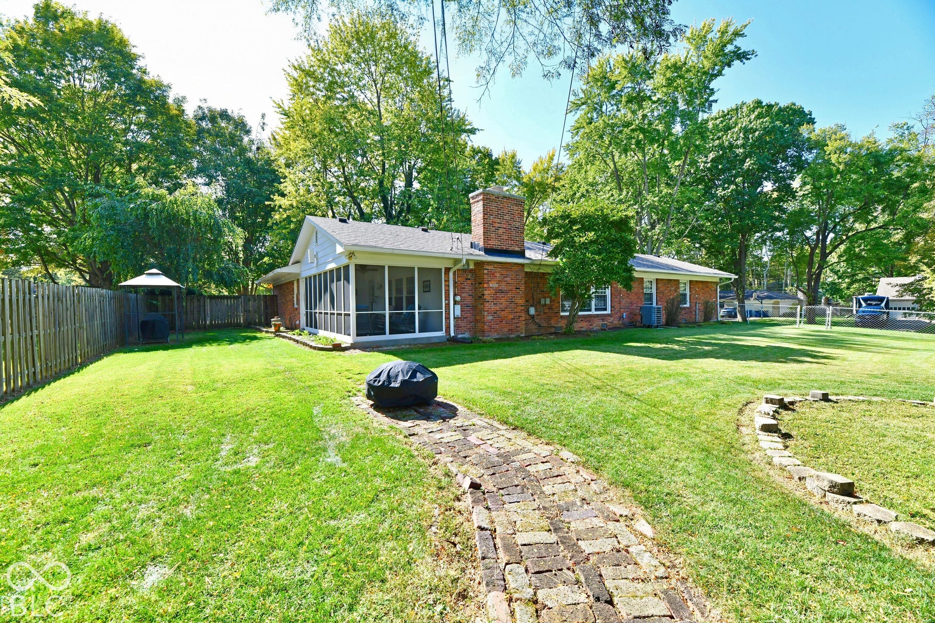 Rear exterior featuring red brick masonry, a screened-in porch, a stone paver walkway, and a fenced yard with mature trees
