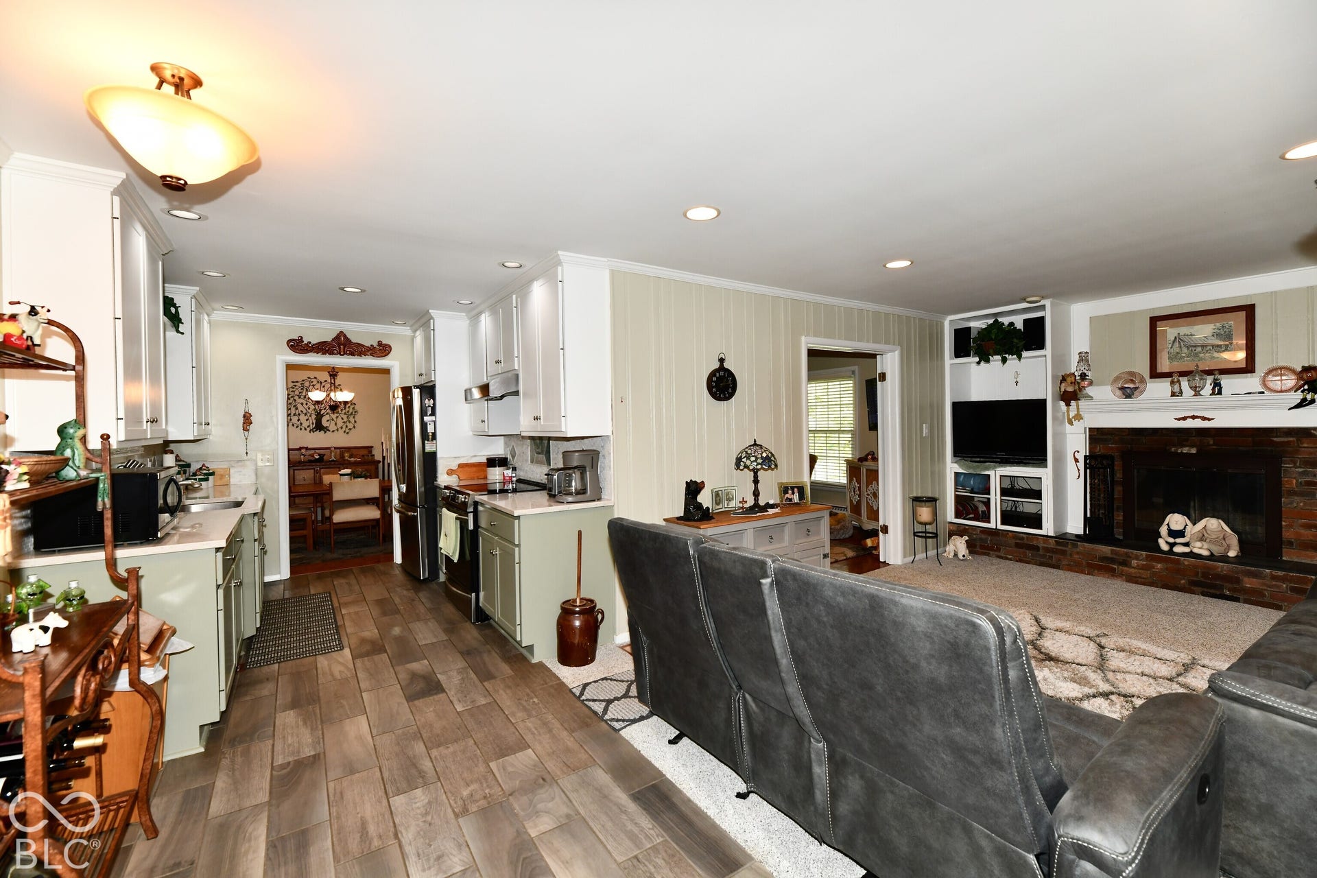 Kitchen featuring light-toned cabinetry, wood-finish flooring, and recessed lighting, paired with a fireplace showcasing a brick surround and built-in shelving