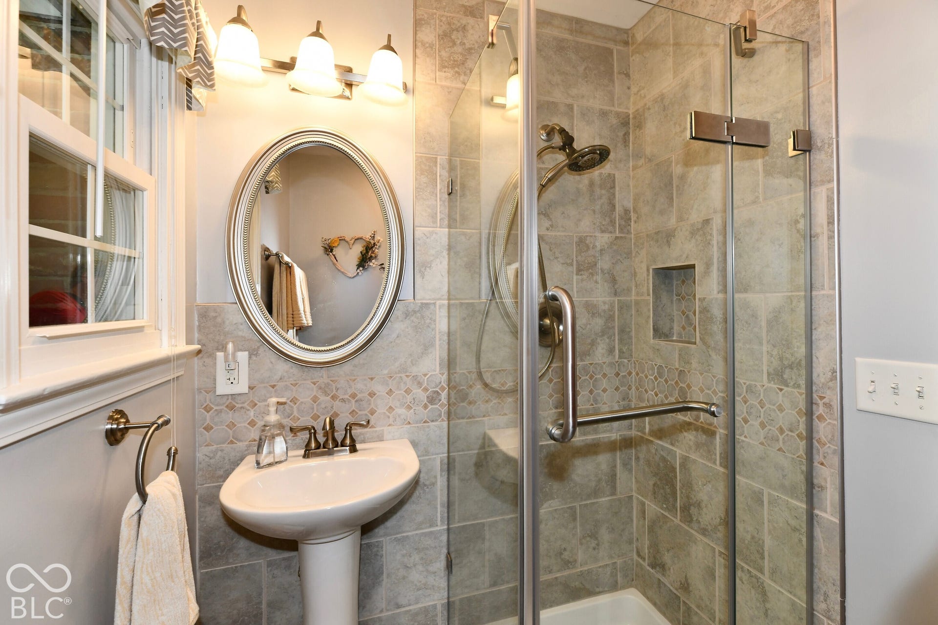 Bathroom featuring a pedestal sink with a metallic faucet, a glass-enclosed shower with tiled walls and an integrated niche, and an oval wall-mounted mirror